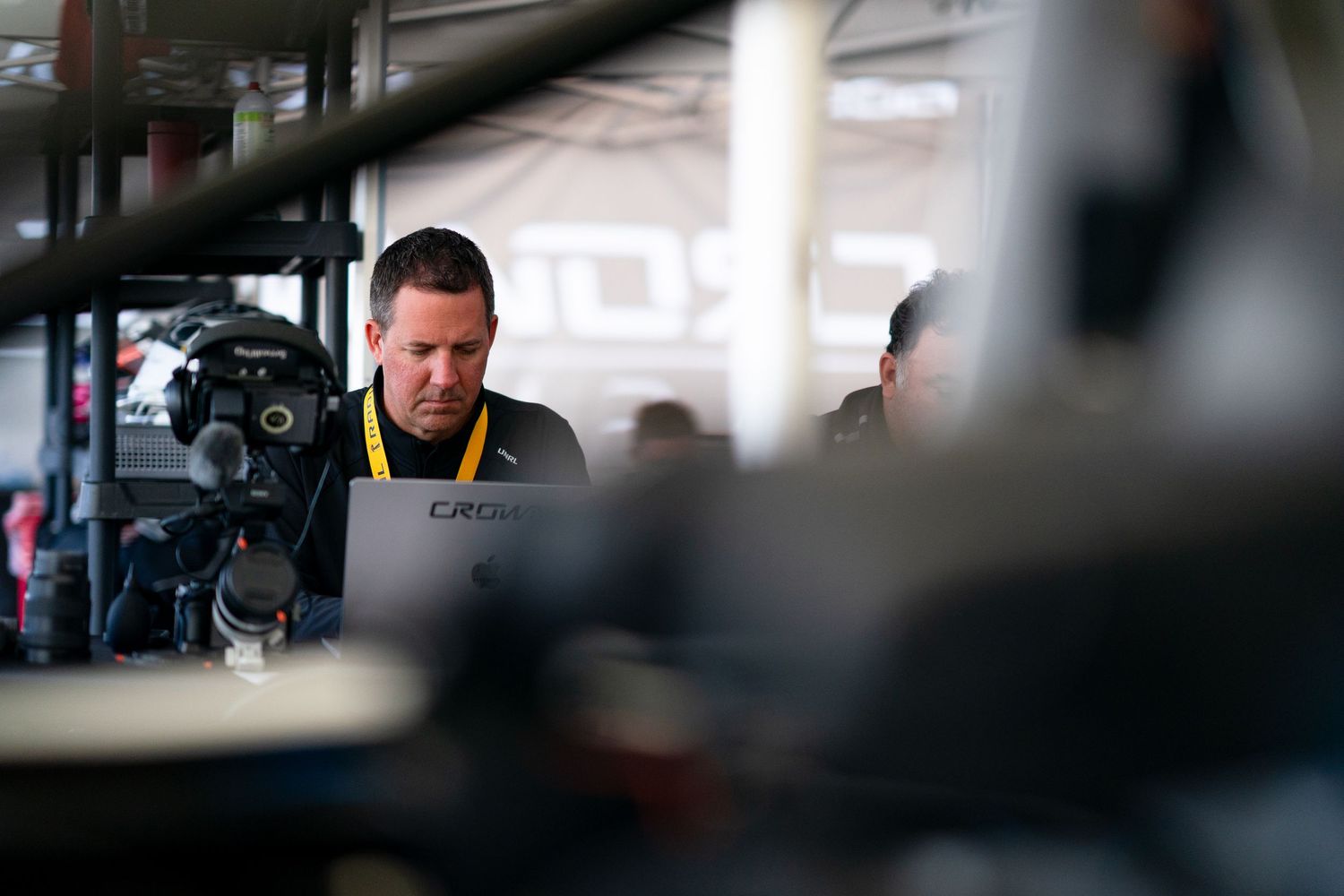Behind-the-scenes view of racing team personnel working in the pit lane area.