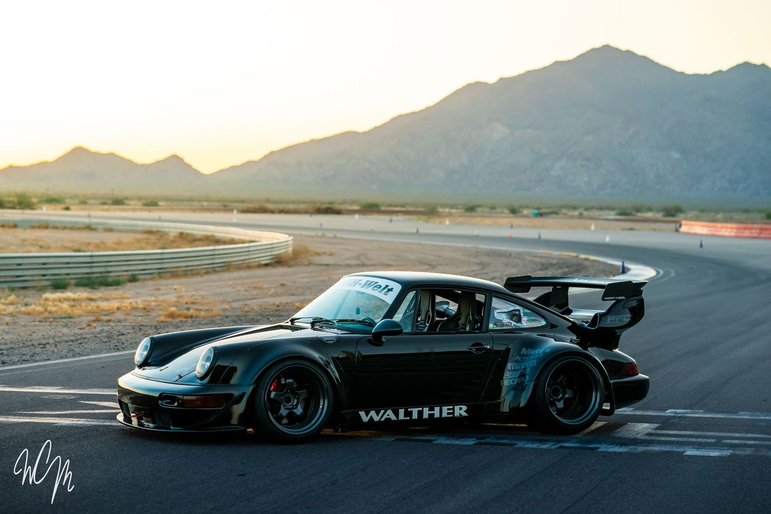 Modified black Porsche 911 race car with Walther livery on desert racetrack.
