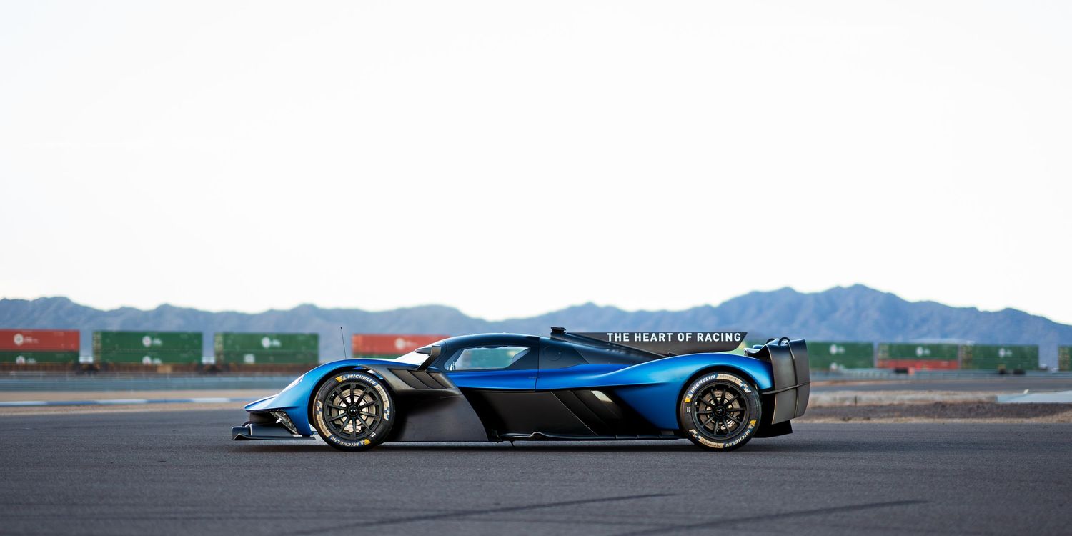 Three racing cars lined up on a track with mountains visible in the background.