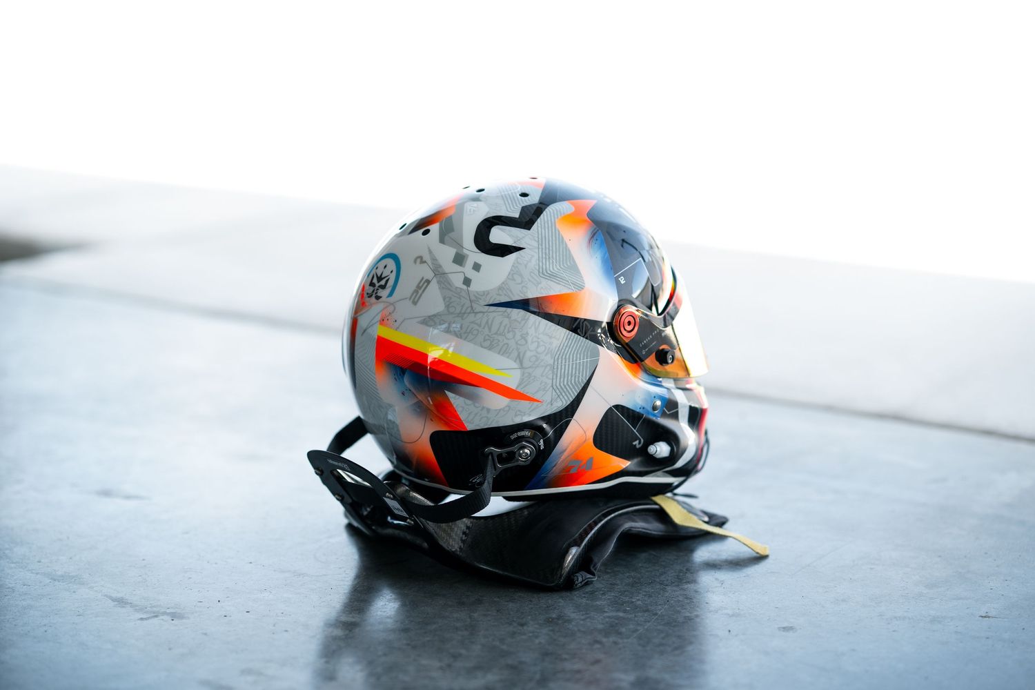 Racing helmet with grey and orange design pattern sitting on black surface.