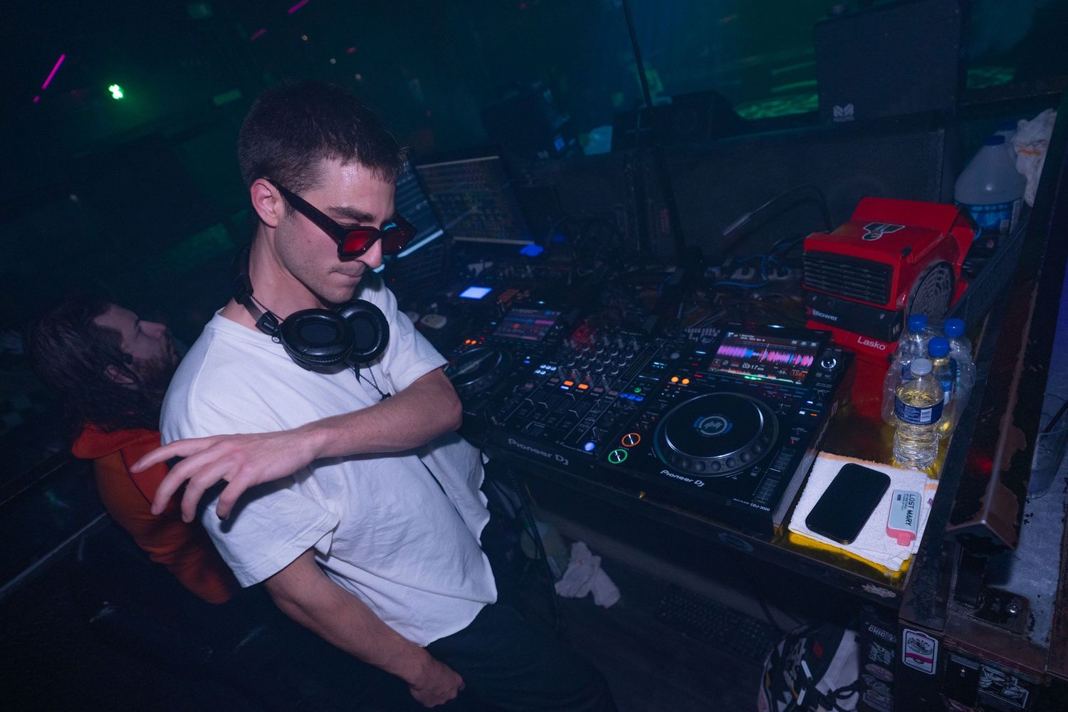 DJ performing at a nightclub with turntables and mixing equipment in a dark environment.