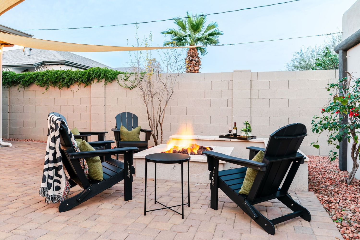 Cozy outdoor patio seating area with fire pit, Adirondack chairs and shade sail overhead.