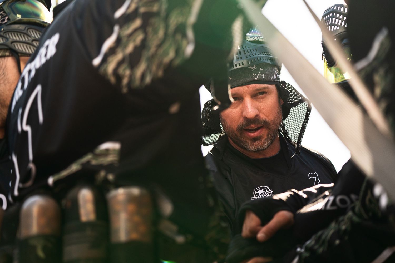 Man in tactical gear and headset communicating with team members during a paintball competition.