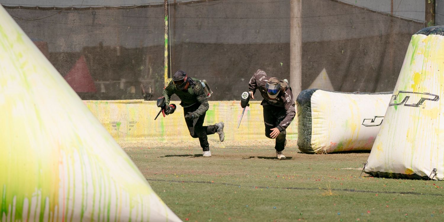 Two paintball players running between yellow bunkers during intense match.