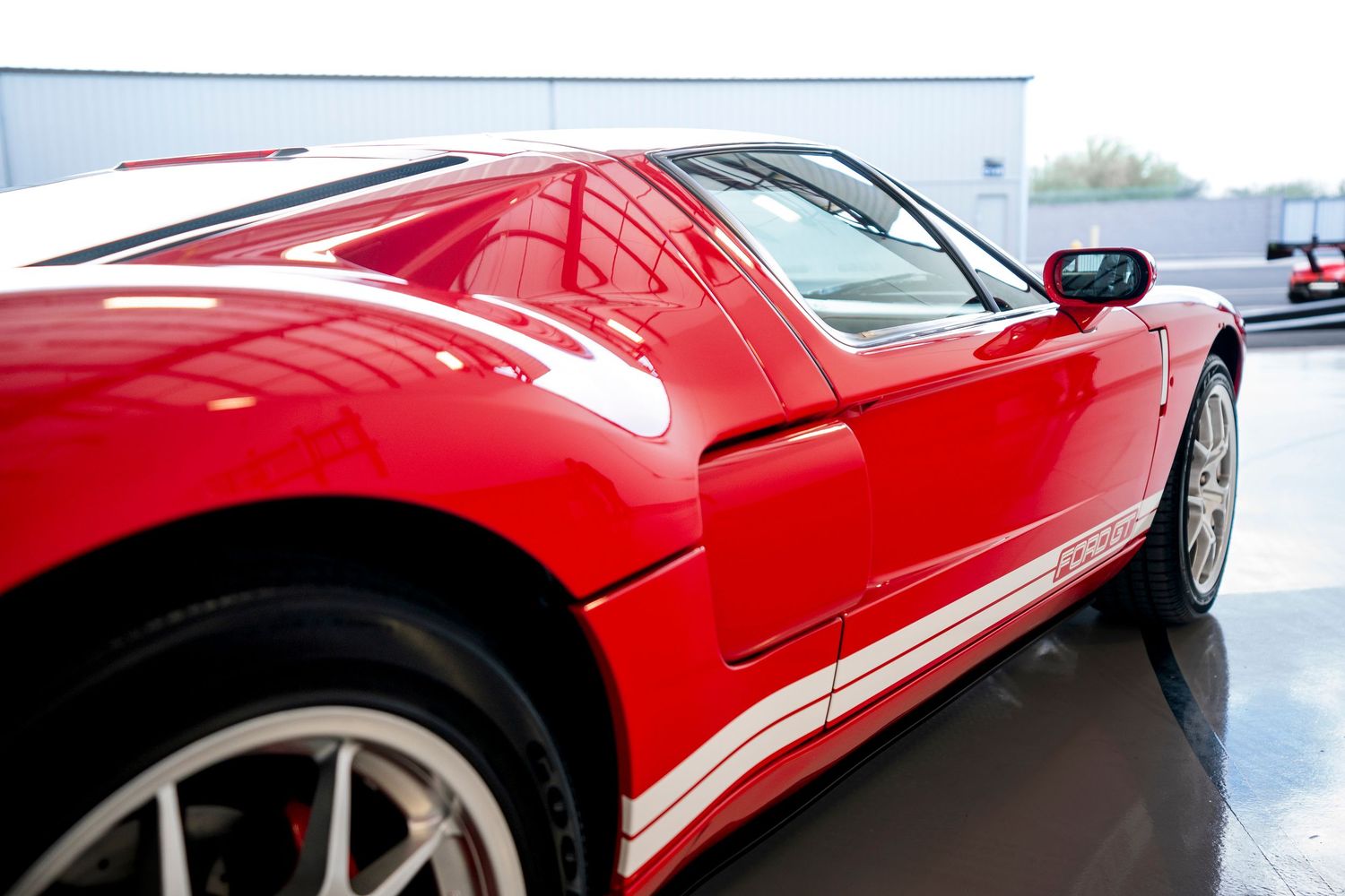 Side profile detail of red Ford GT showing sleek bodywork and white racing stripe.