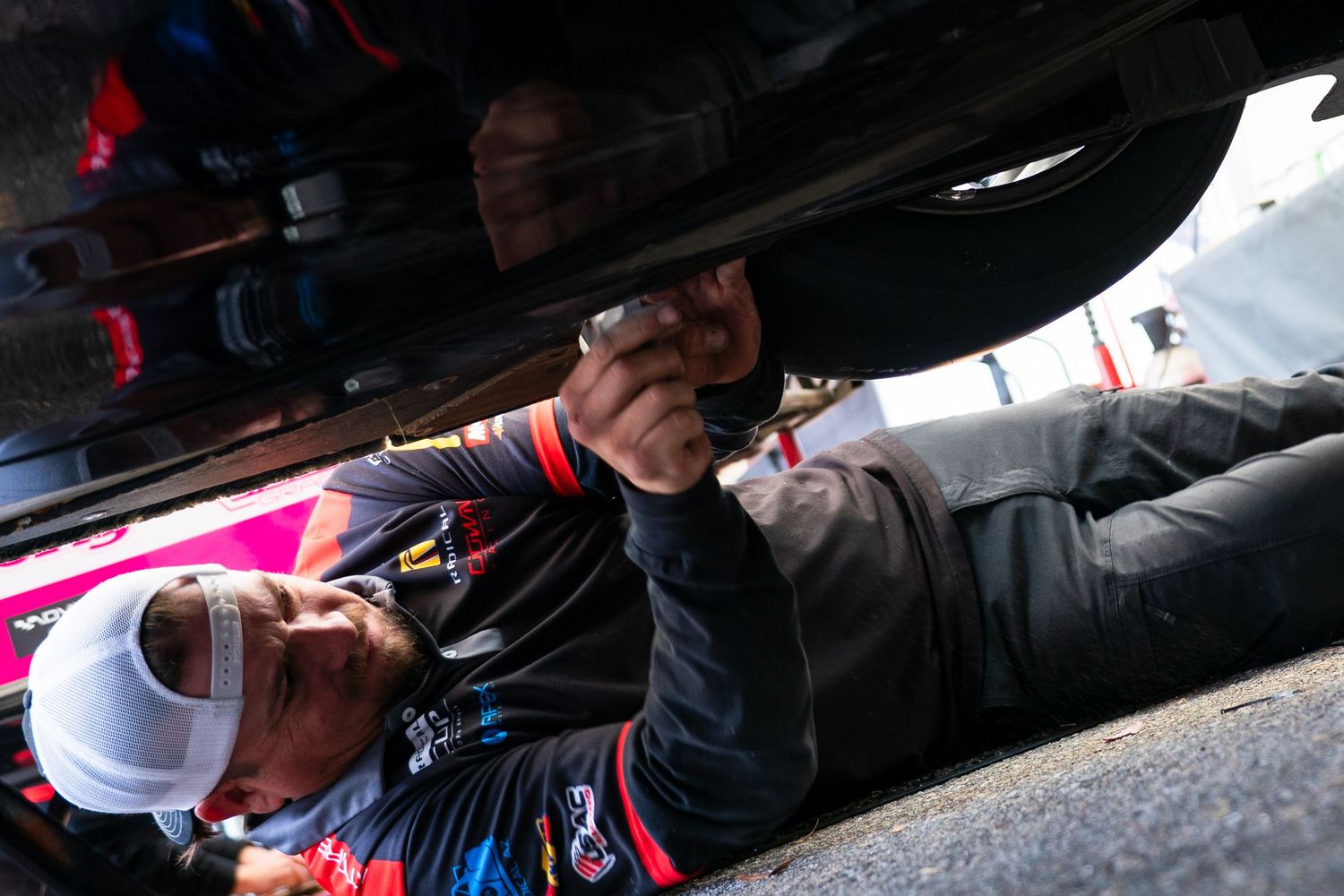 Detailed shot of technicians performing adjustments on racing vehicle undercarriage.