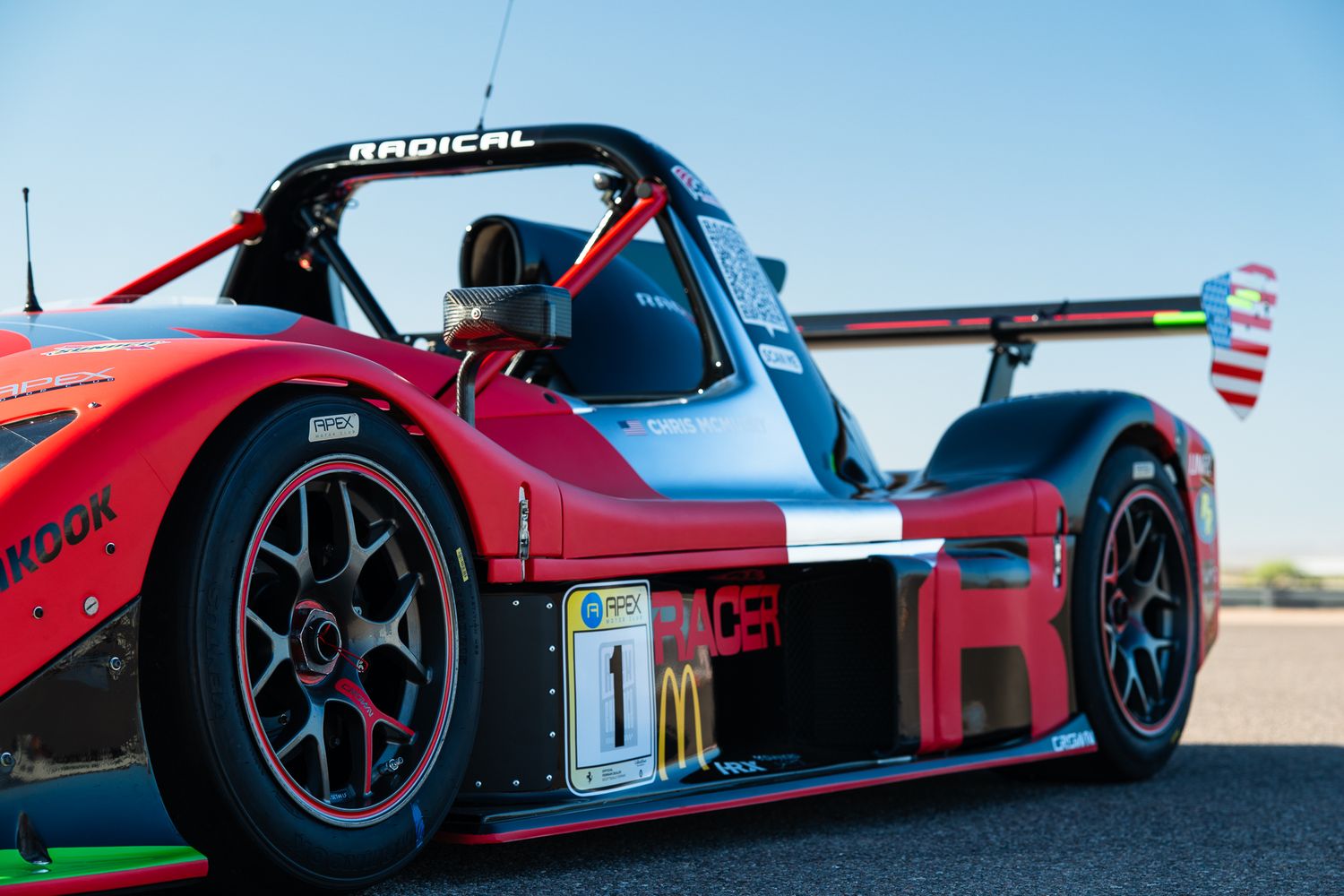 Side profile of red Radical SR3 race car with black wheels on track.
