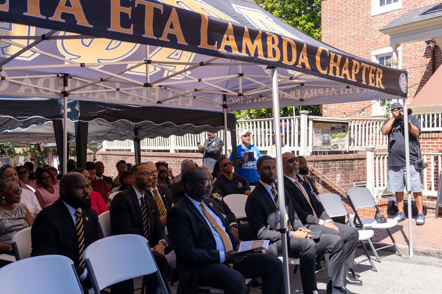 Crowd gathers under Eta Eta Lambda Chapter tent during outdoor event.
