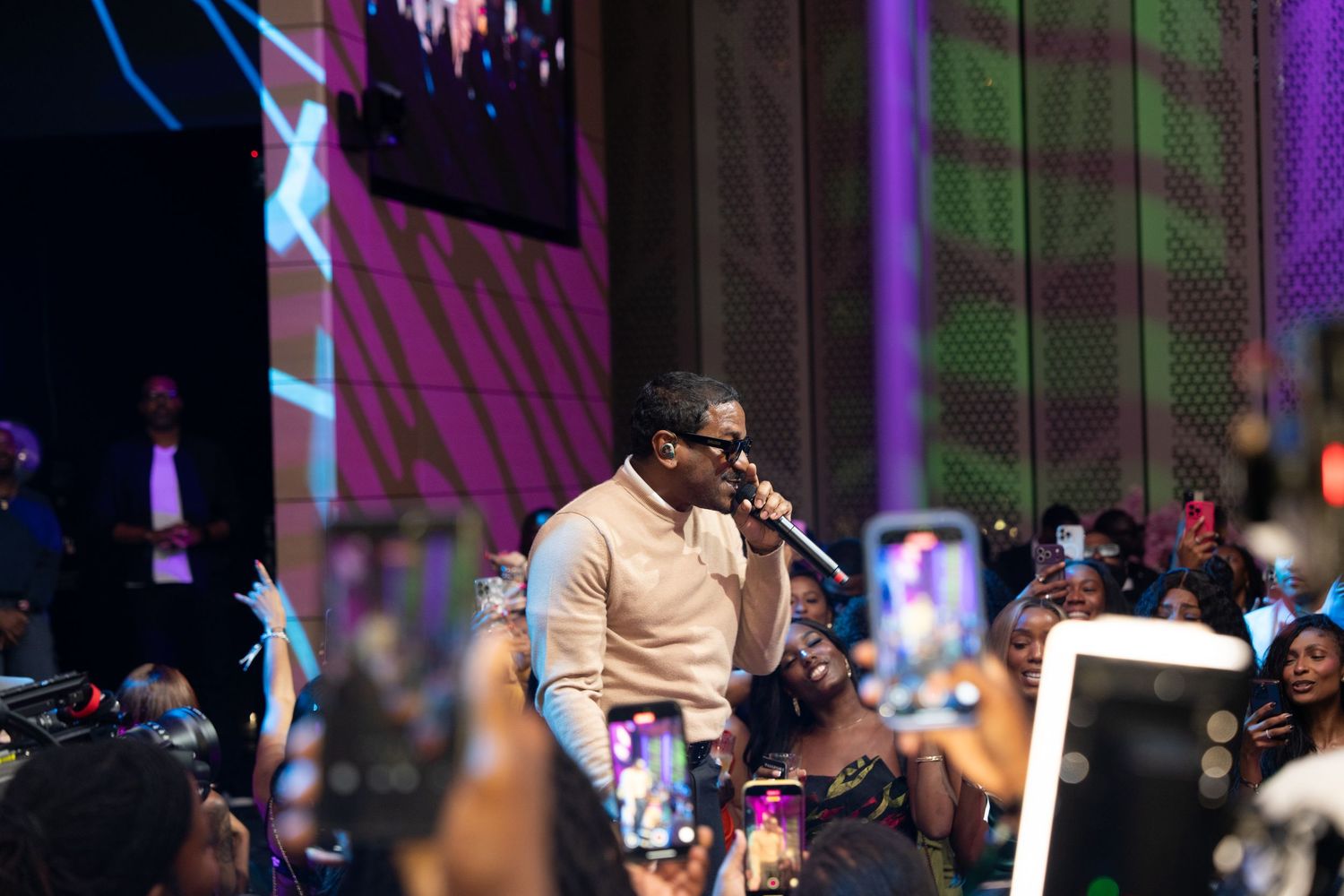 Concert performer on stage with purple lighting and crowd in background.