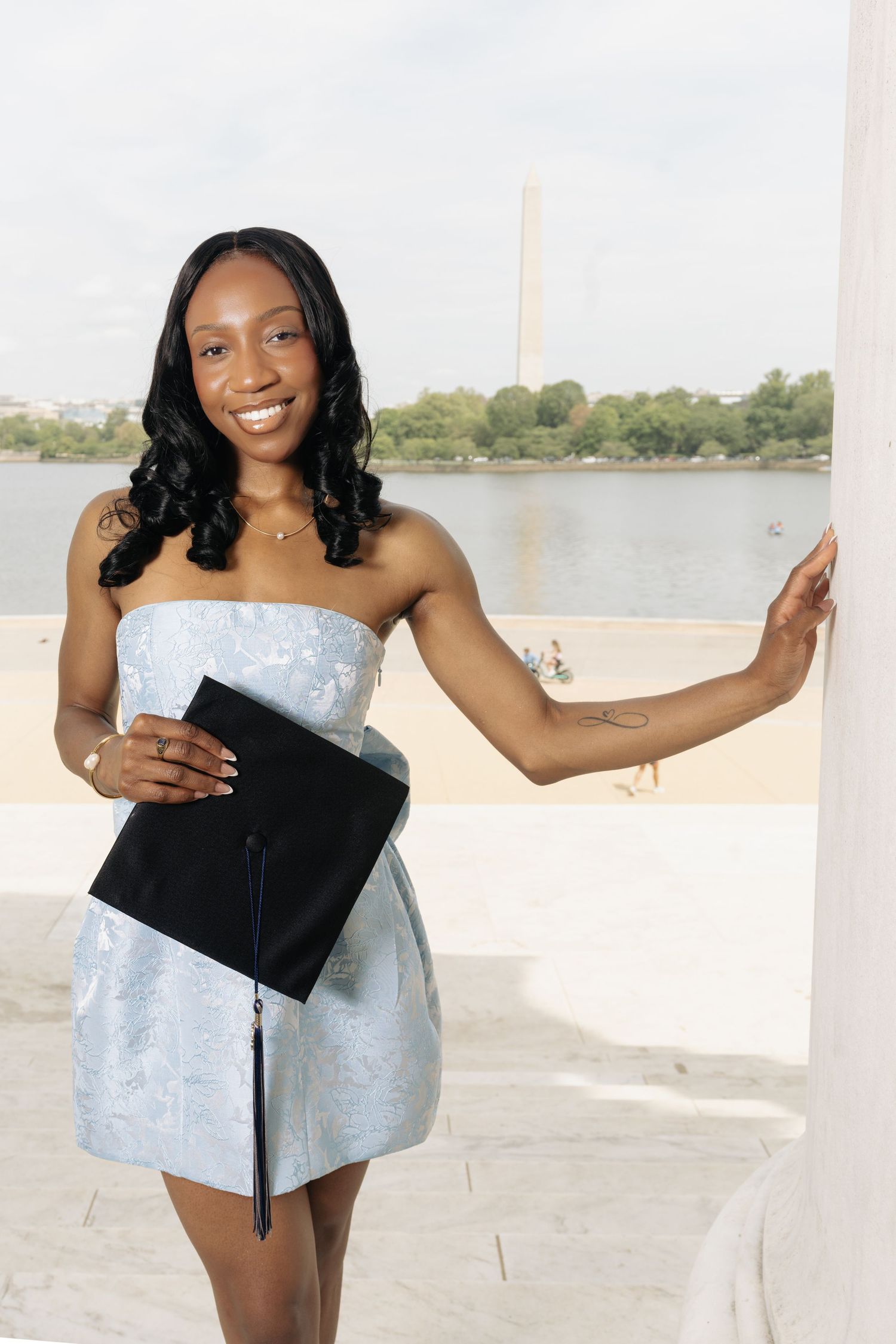 Graduation photoshoot on waterfront featuring light blue dress and diploma.