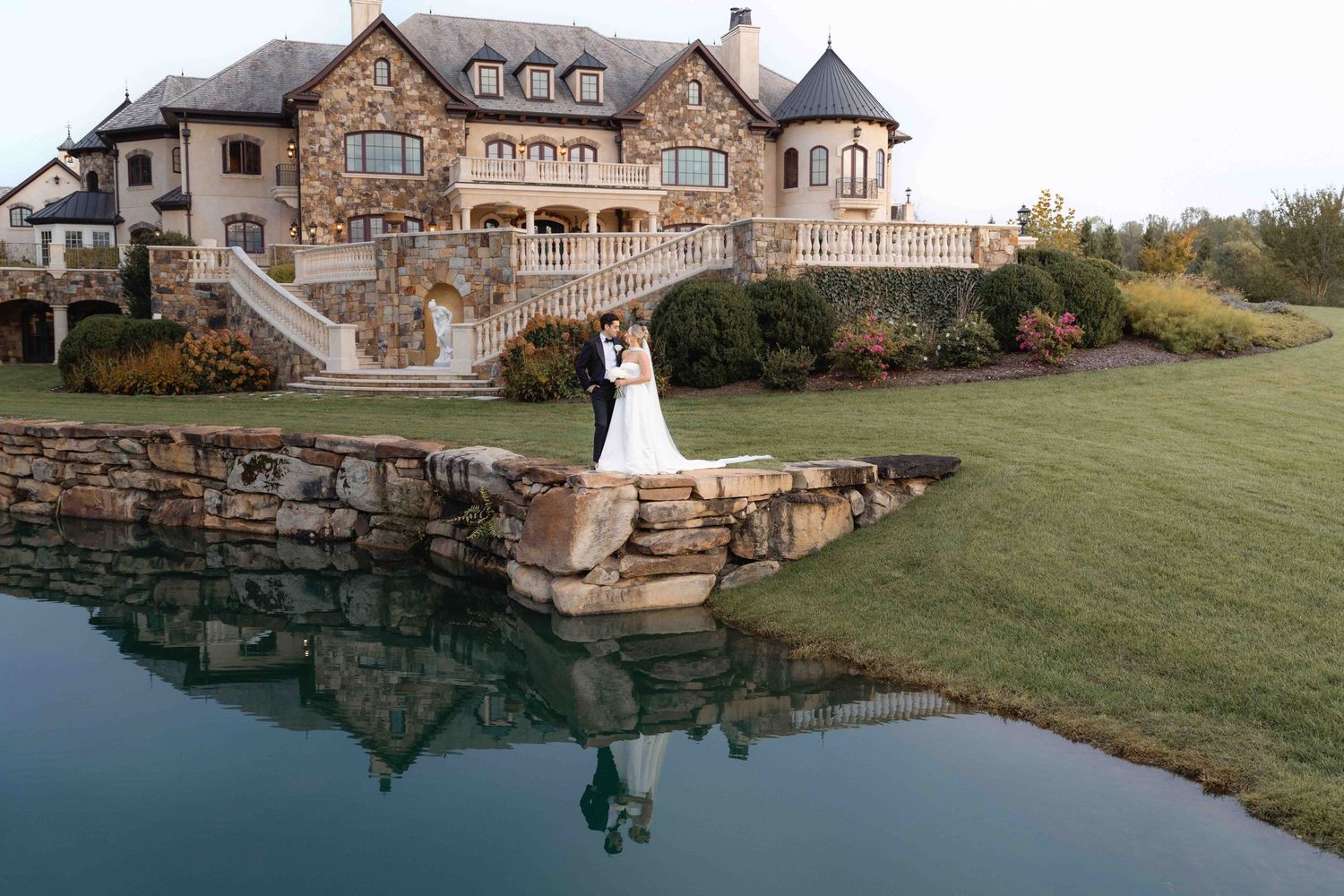 Luxurious stone mansion with reflective pool creating a mirror image in the water.