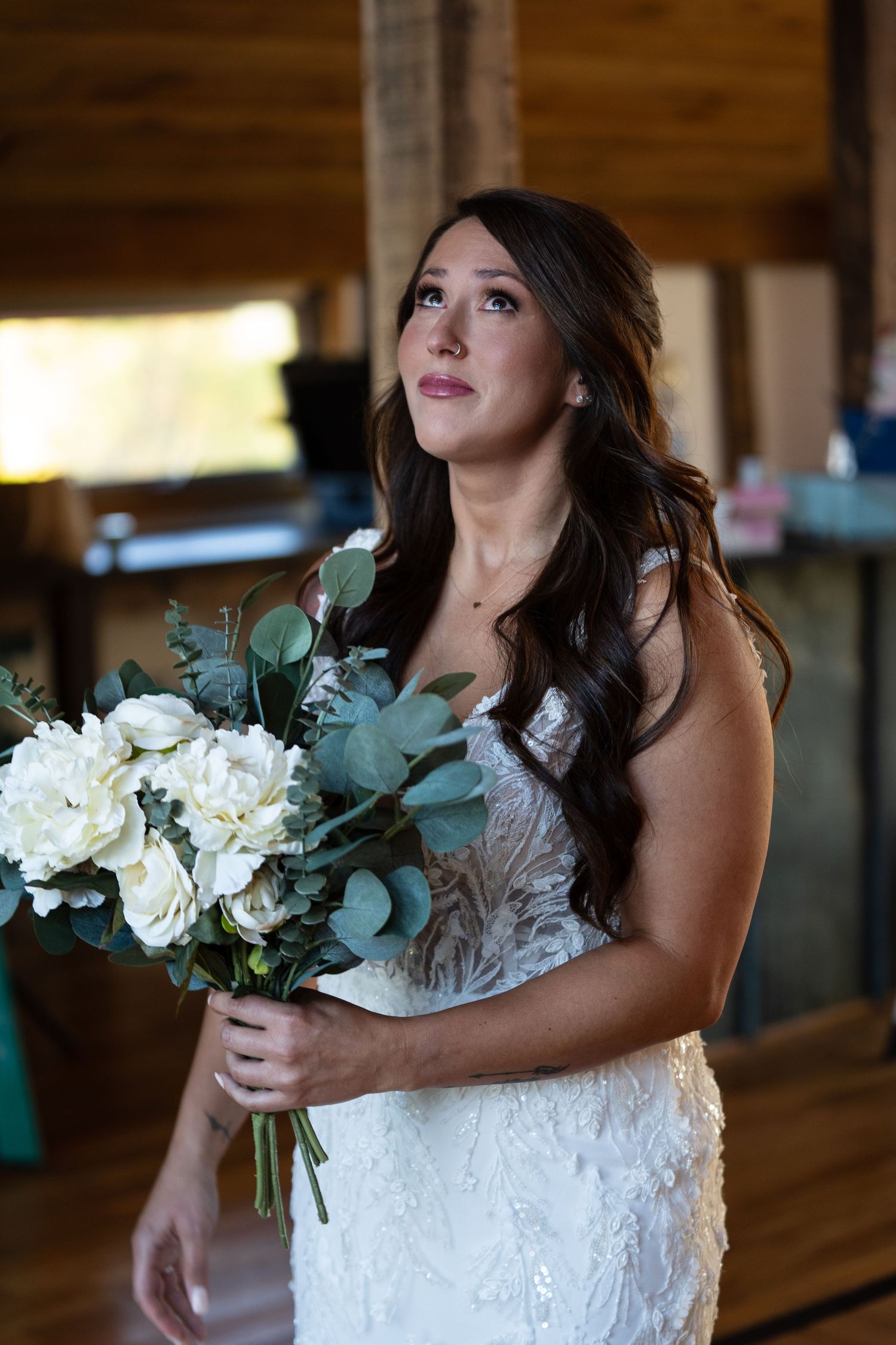 Bride holding an elegant white and green floral bouquet in a rustic wooden venue.