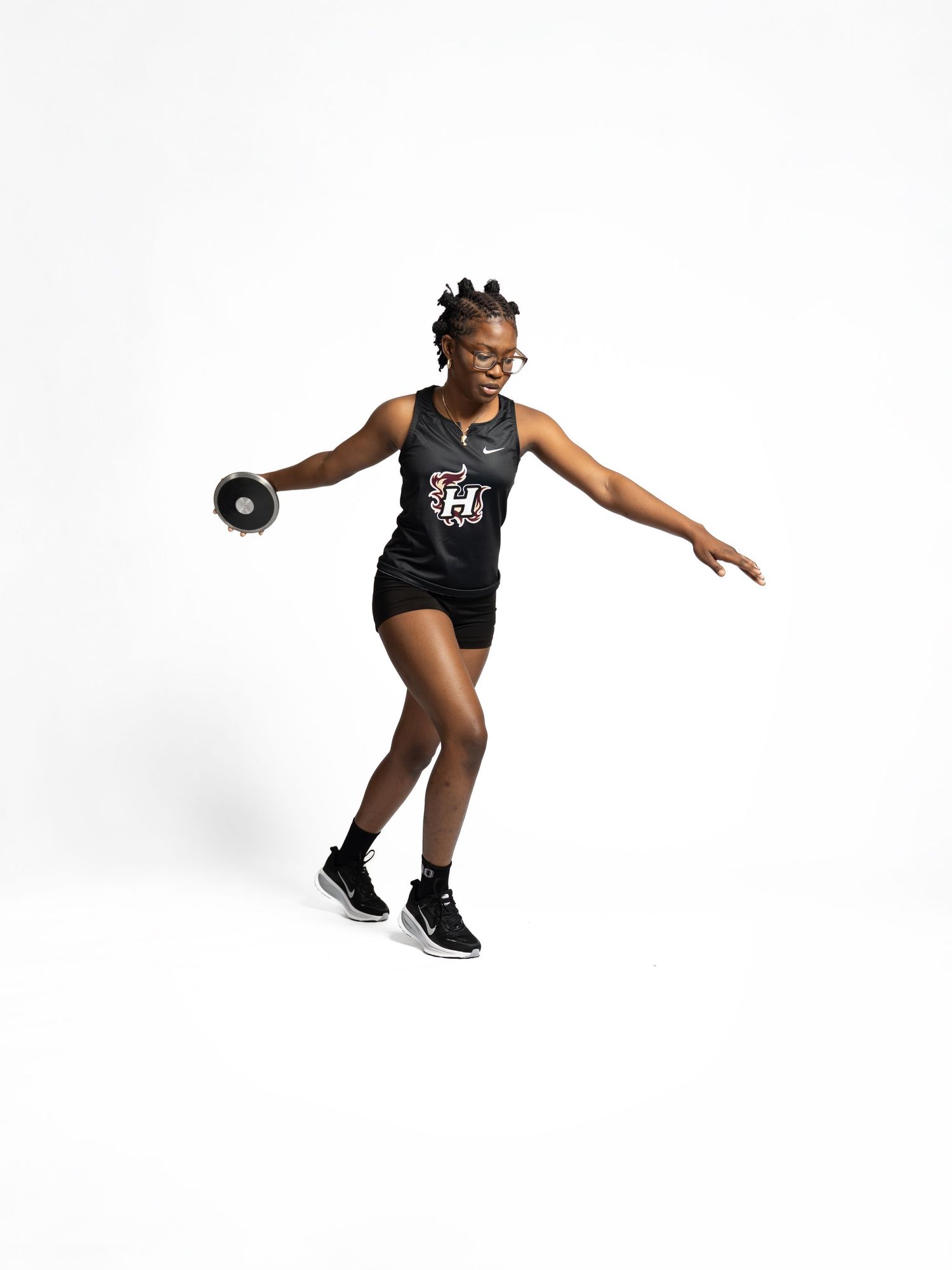 Athletic person in black workout gear performs dynamic discus throwing motion against white background.