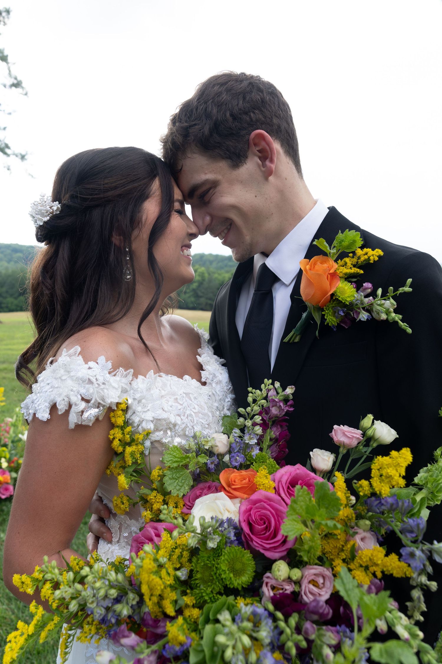 Romantic wedding couple embraces among vibrant floral arrangements with mountains in distance.