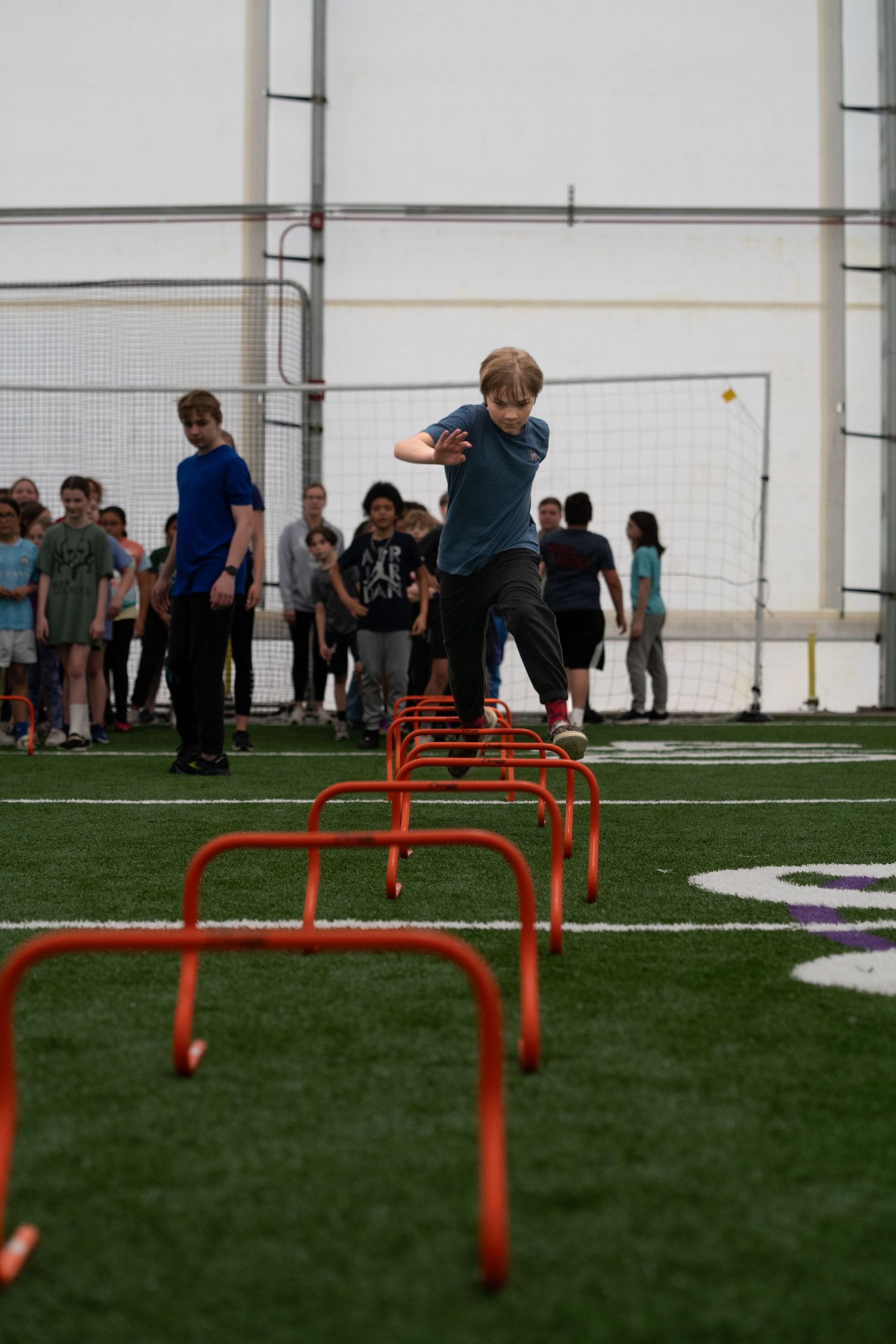 Person jumping over orange hurdles on an indoor turf field during training.