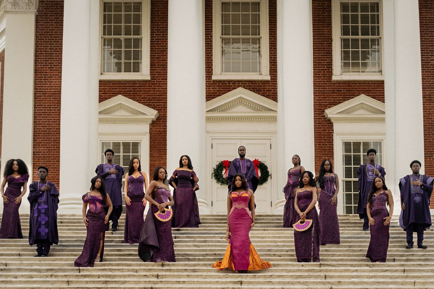 Wedding party lined up on white columned building steps wearing purple formal attire.