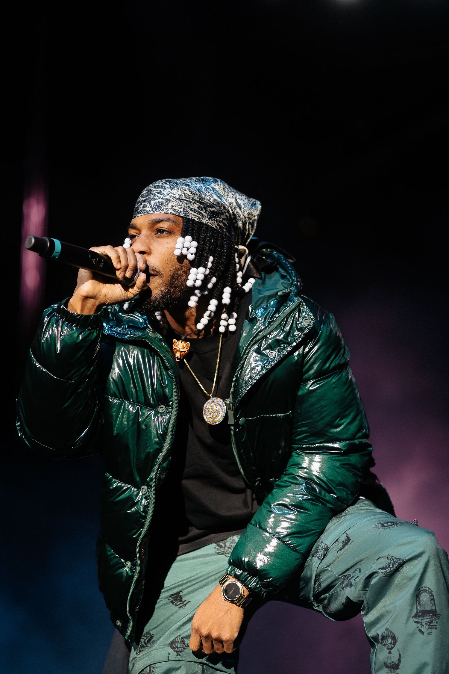 Artist performs energetically in shiny green jacket under blue stage lights.
