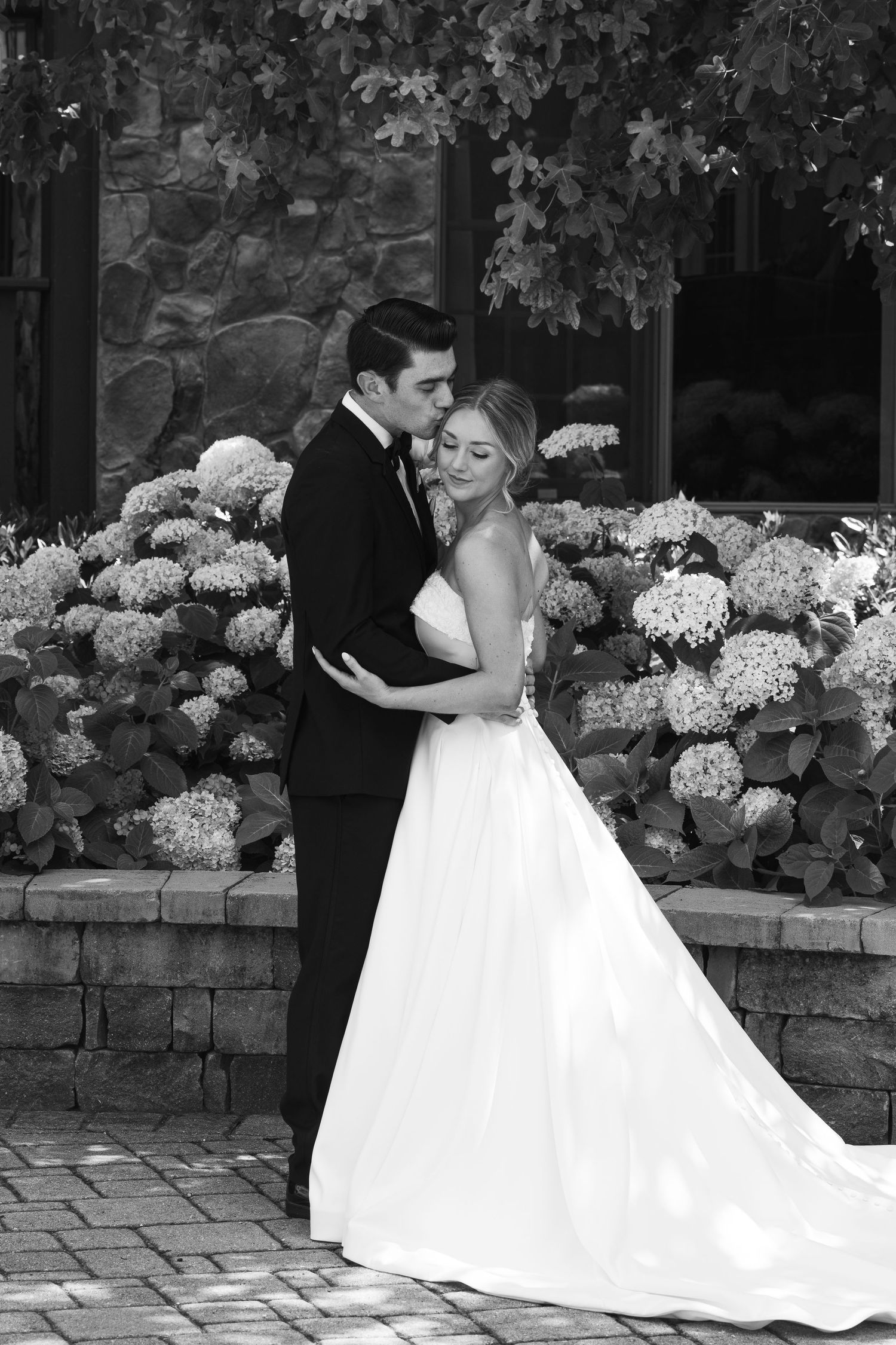 Wedding couple posing by stone wall with white hydrangea flowers.