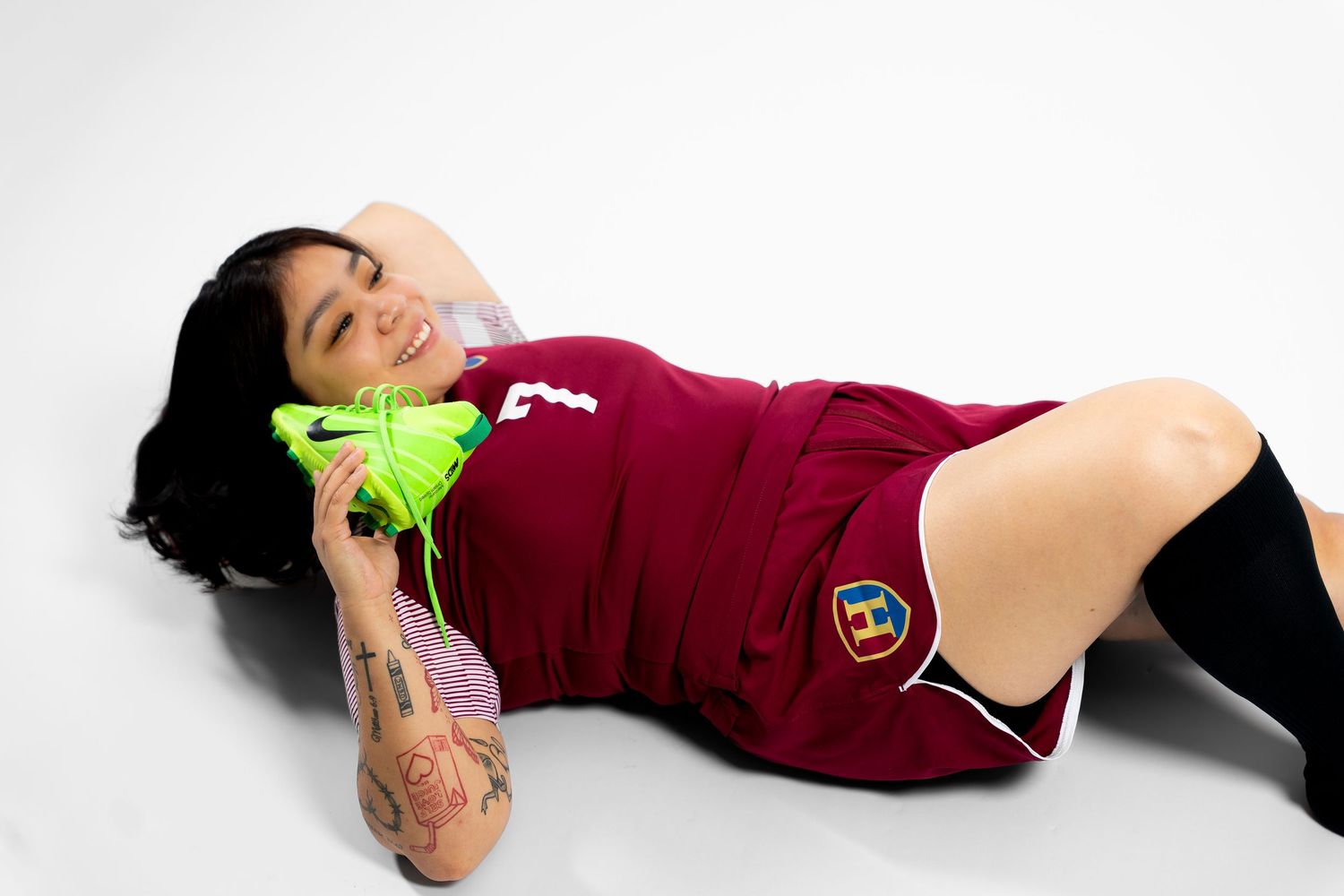 Soccer player in maroon uniform lying on white studio floor with neon accessories.