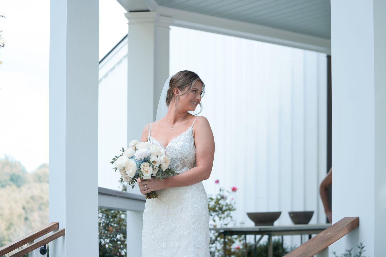Elegant wedding party in white and teal dresses gather on a covered porch for formal photos.