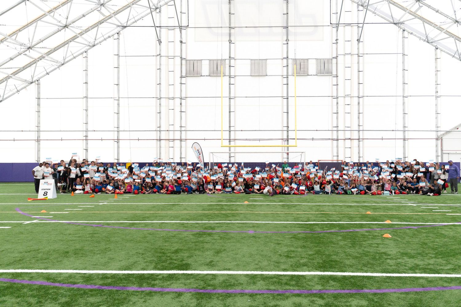 Large group gathered on an indoor football field under a white dome structure.