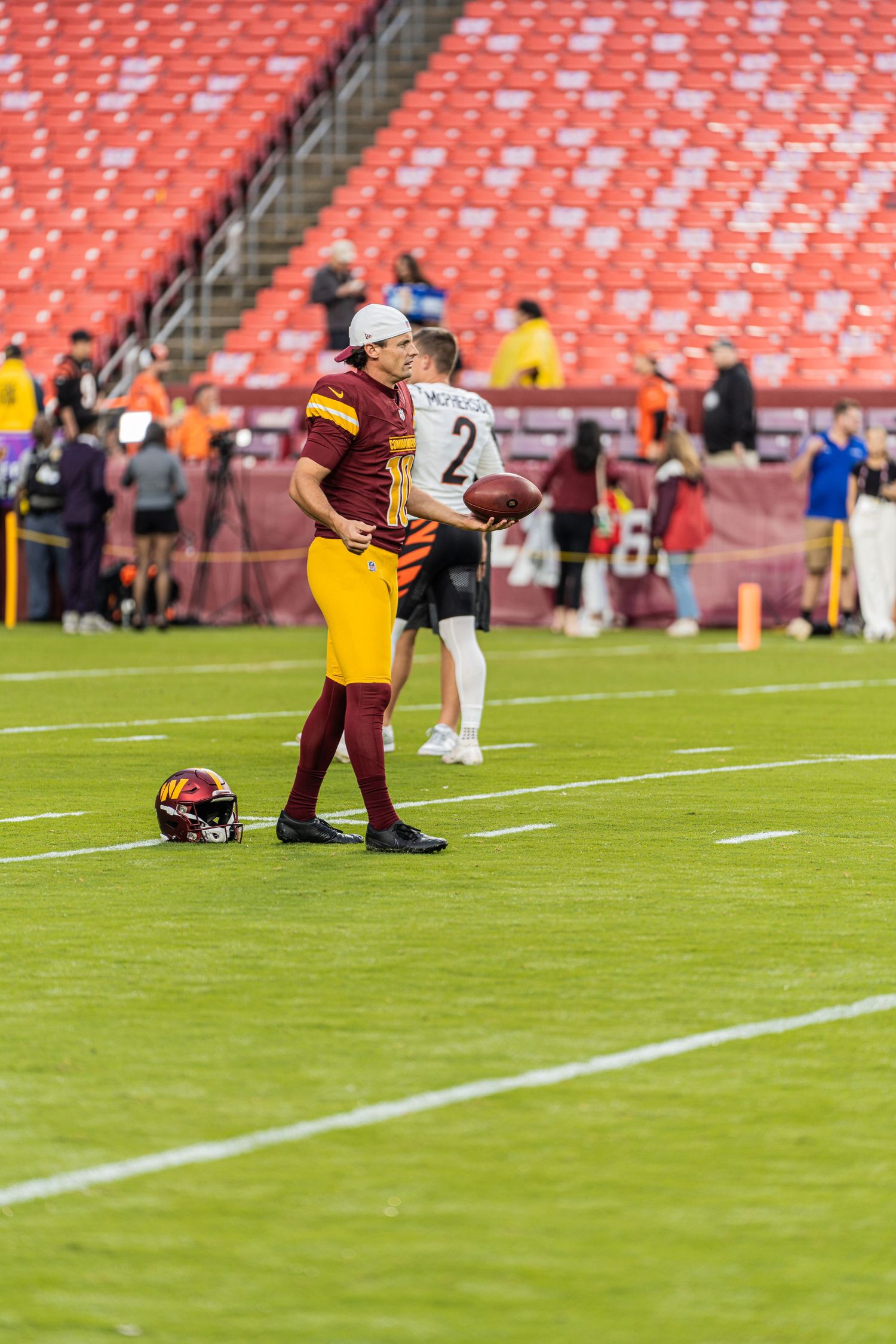 Players stretching on football field with empty red stadium seats visible in background.