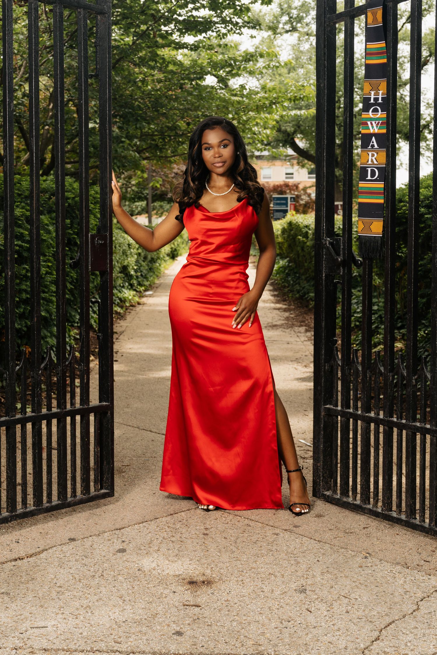 Red satin dress photoshoot by ornate black metal gates in an outdoor setting.