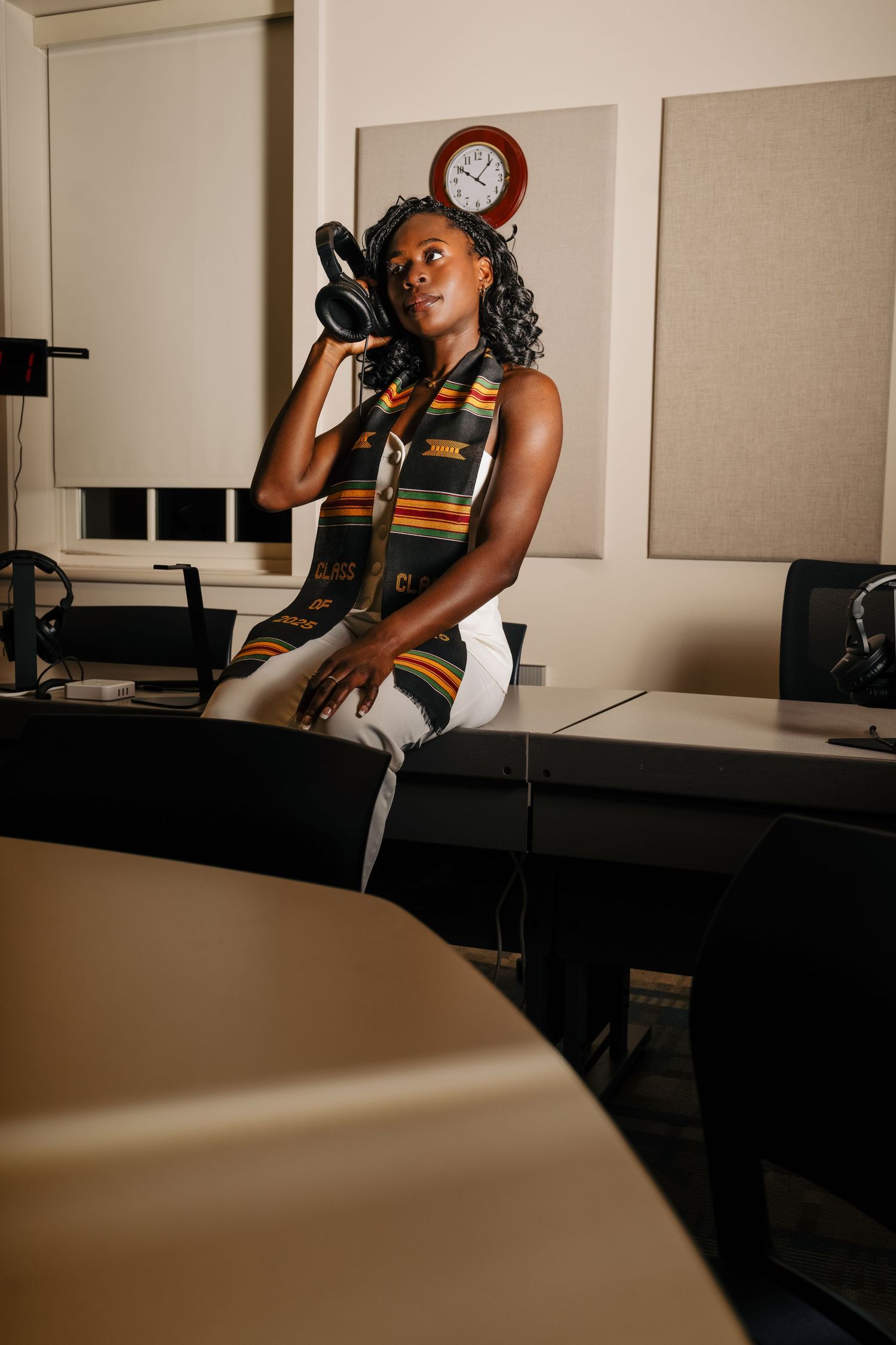 Person in professional attire speaking on phone in office setting with clock visible.
