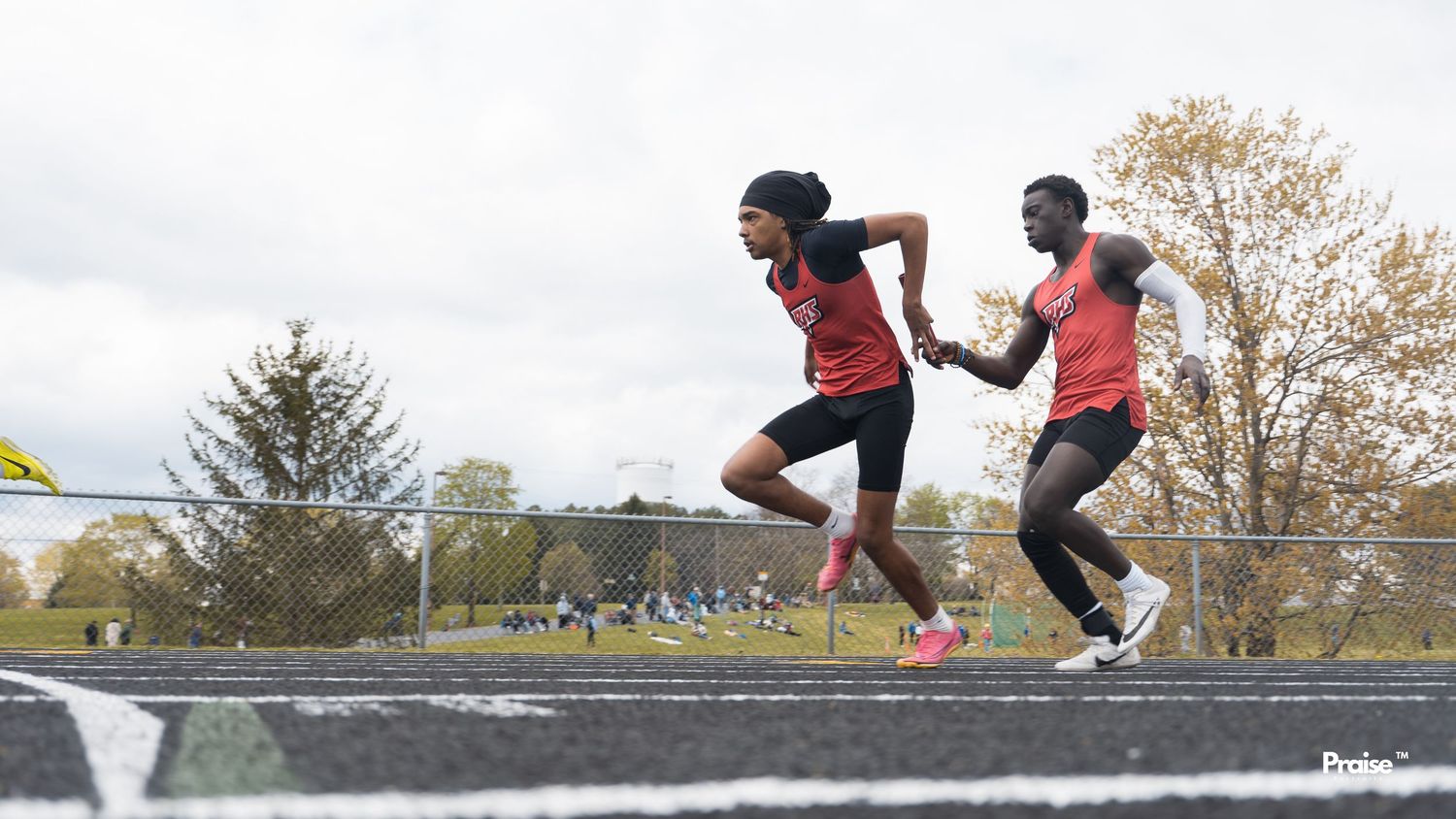 Track athletes competing in hurdle races on an outdoor track during overcast weather.