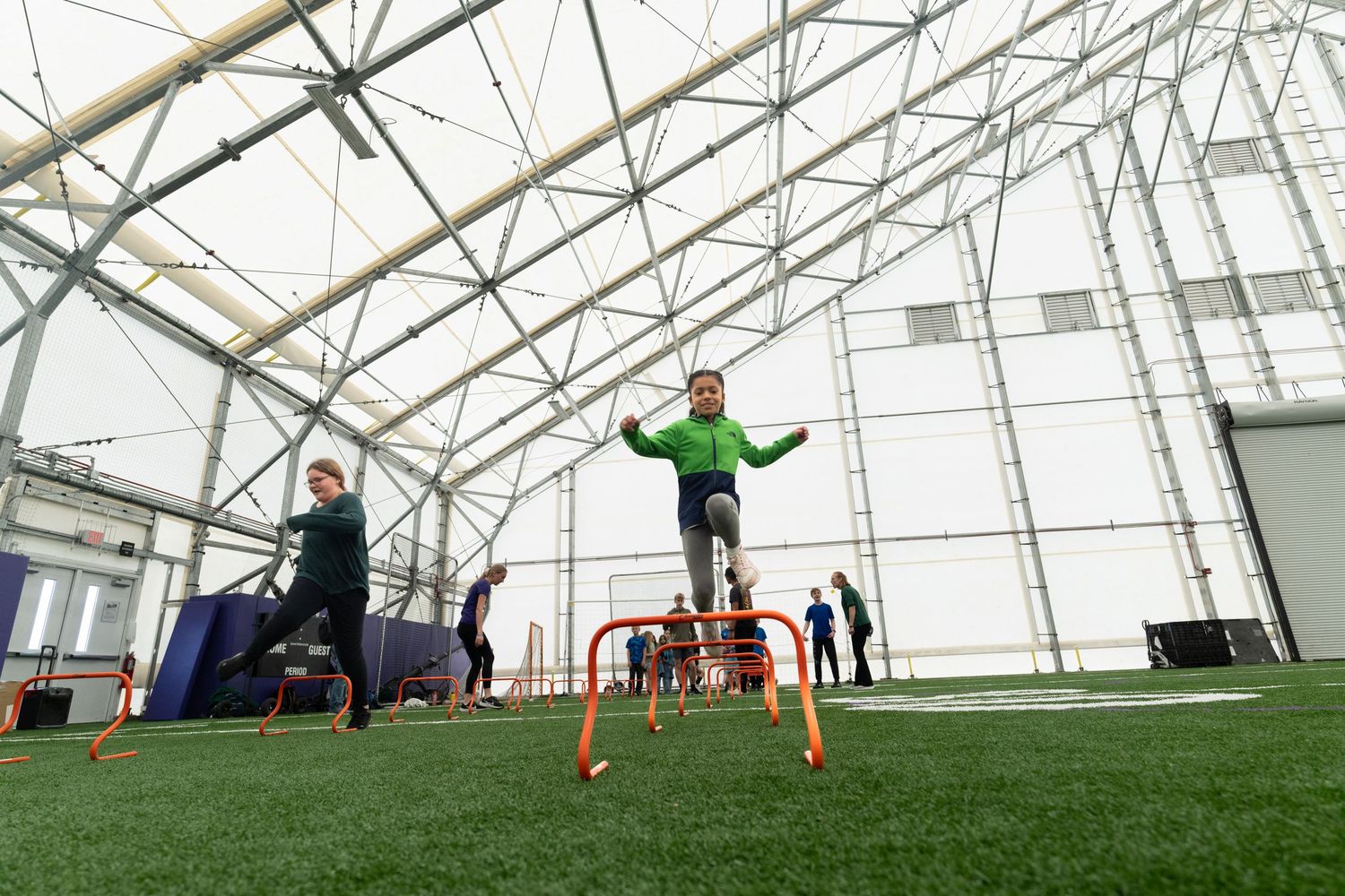 Athletes perform agility drills inside a modern indoor sports facility with artificial turf.