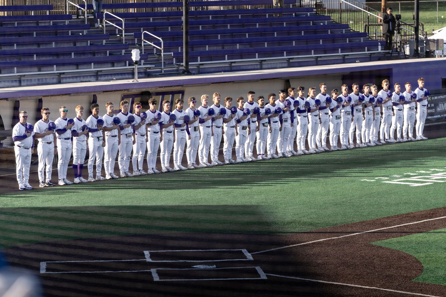 Baseball team lined up along baseline in white uniforms during game ceremony.