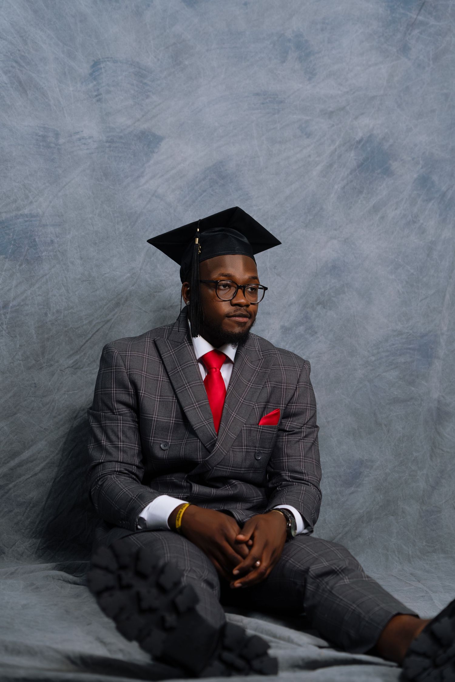 Graduate in pinstripe suit and red tie poses against gray backdrop for professional portraits.