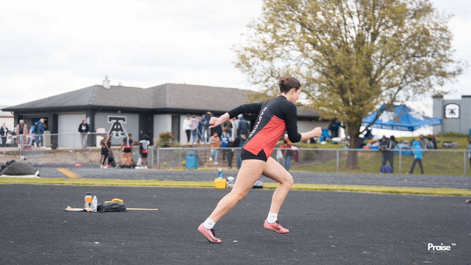 Athletes competing in hurdle races on an outdoor track with spectators watching in the background.