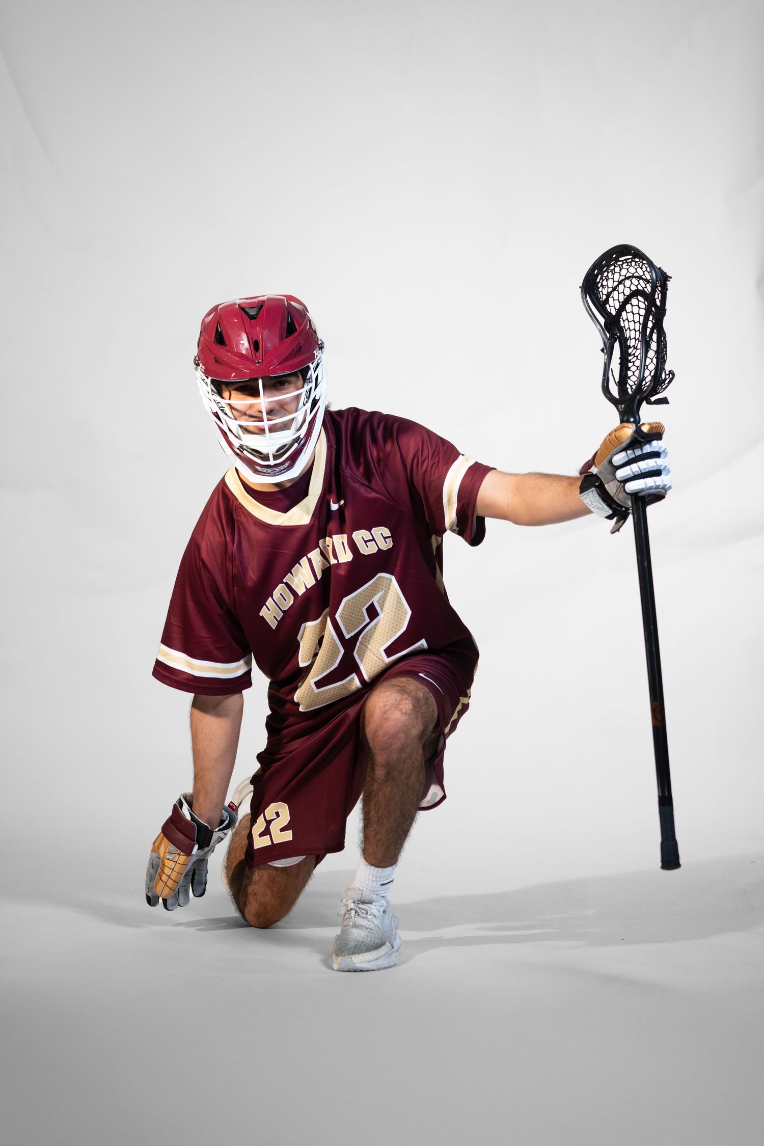Lacrosse player in maroon jersey and helmet demonstrates ground ball techniques on white background.