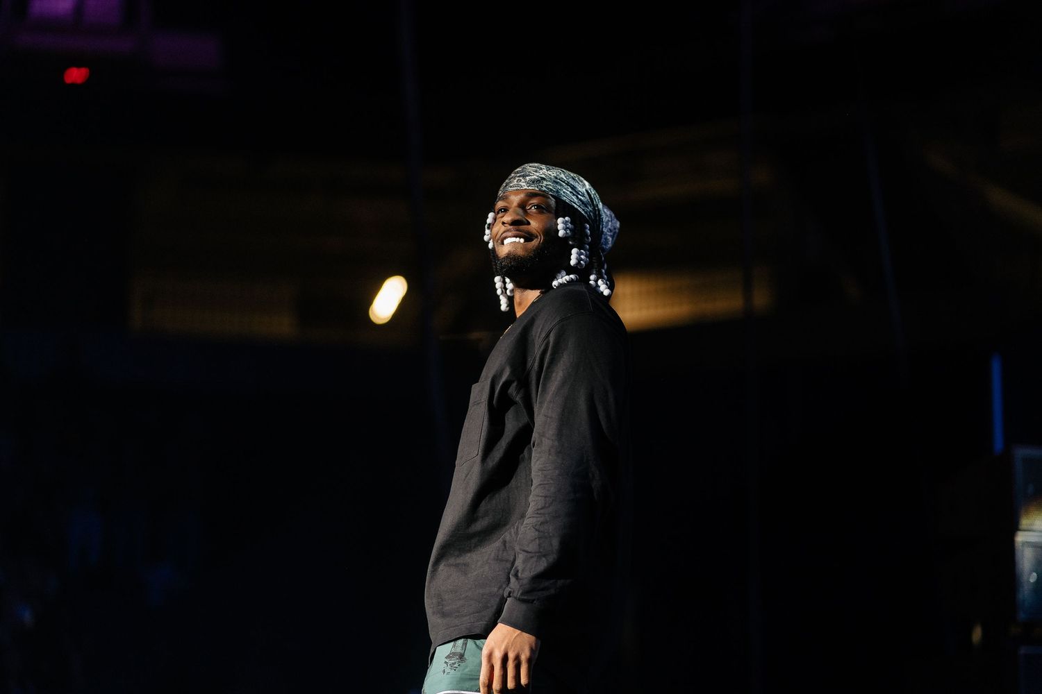 Performer in black outfit energetically moves on dimly lit stage.