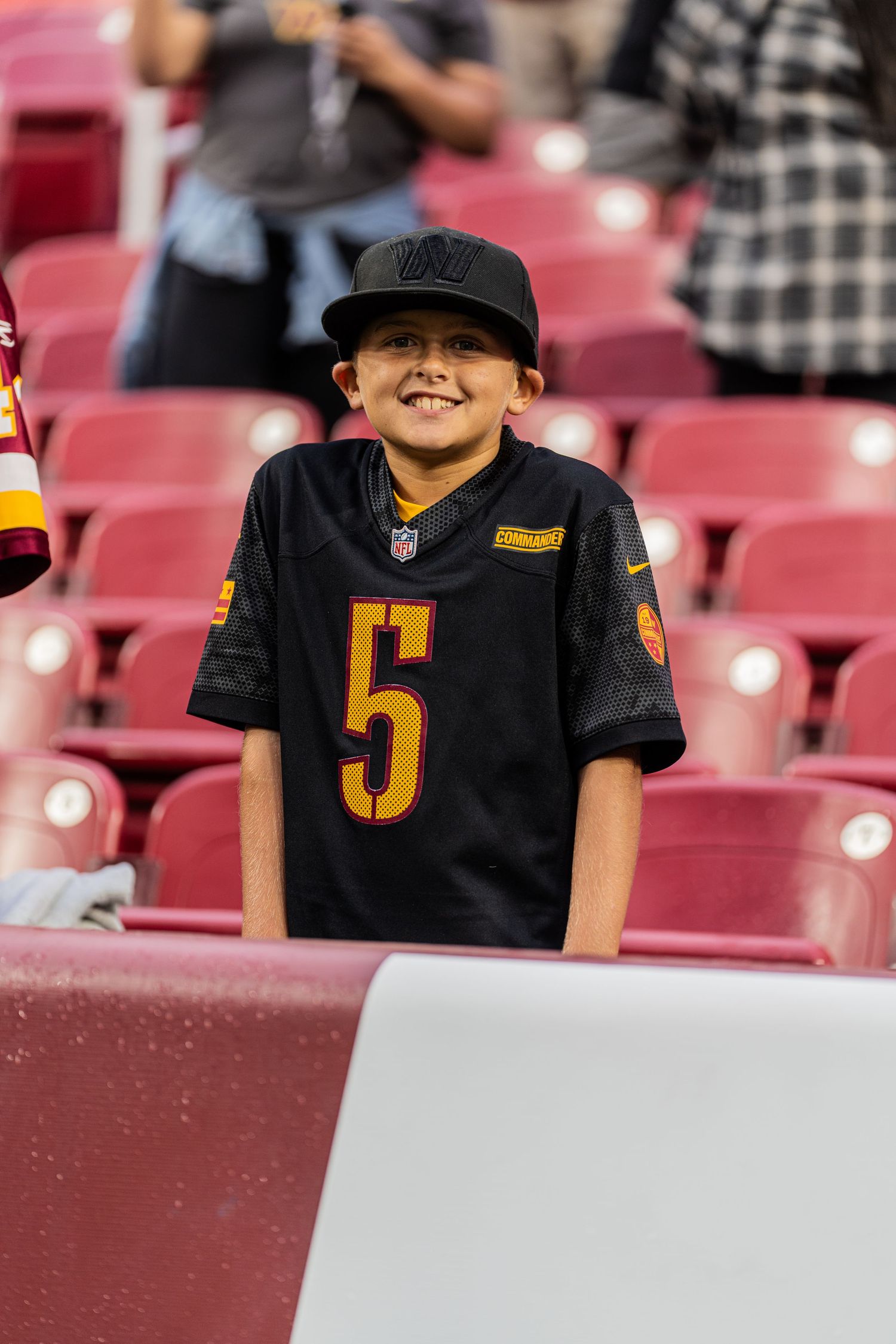 Fans wearing black and gold jerseys seated in stadium bleachers with red seats.