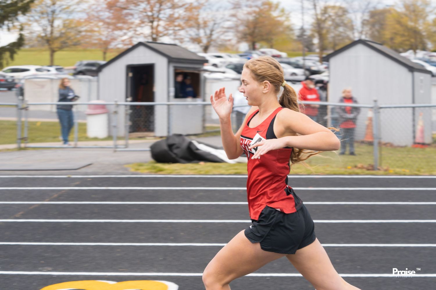 Athletes competing in track events wearing red and black uniforms on an outdoor running track.