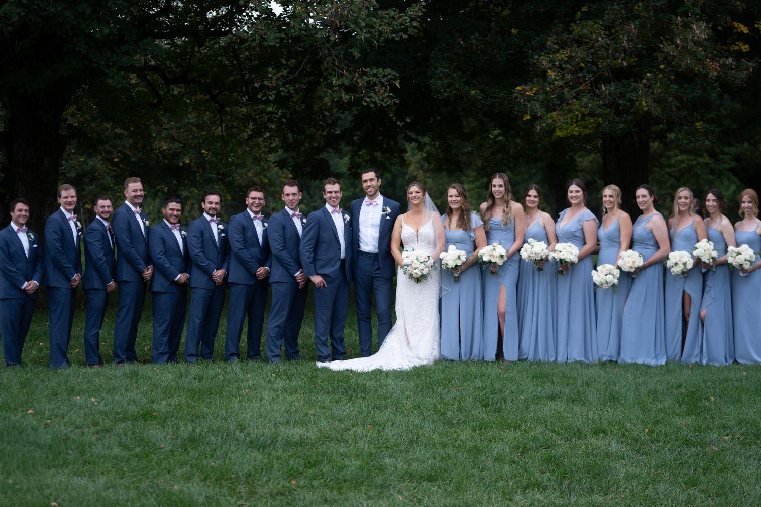 Wedding party in navy and light blue attire poses together outdoors.