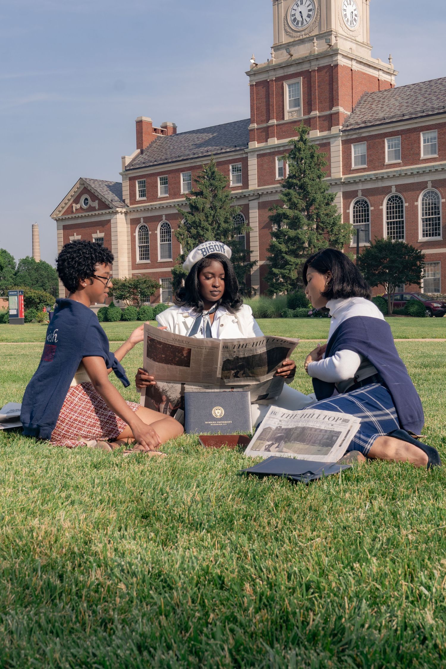 College students studying outdoors on campus lawn with clock tower and brick buildings in background.