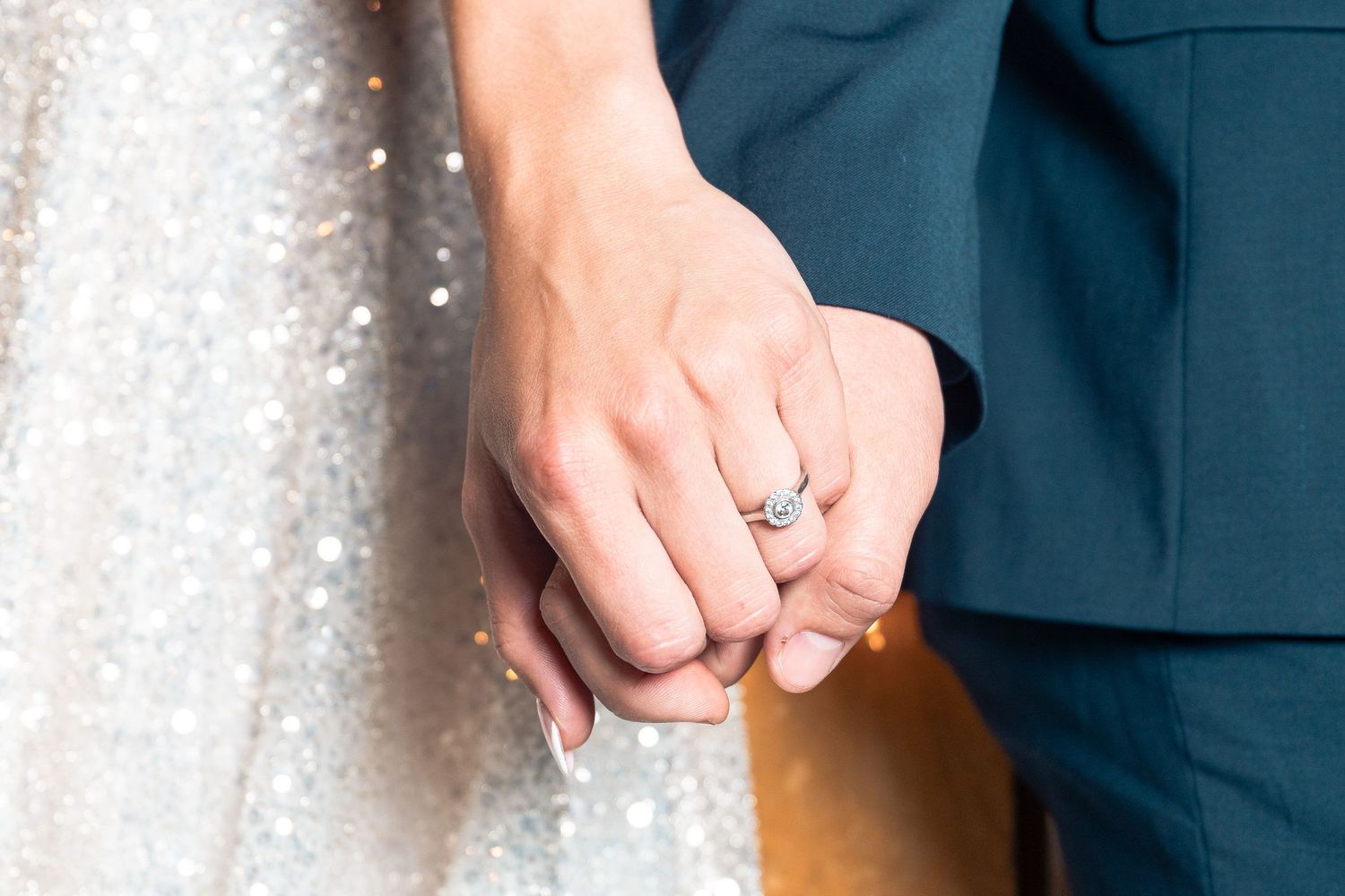 Close-up shot of hands with engagement ring against sparkly background.