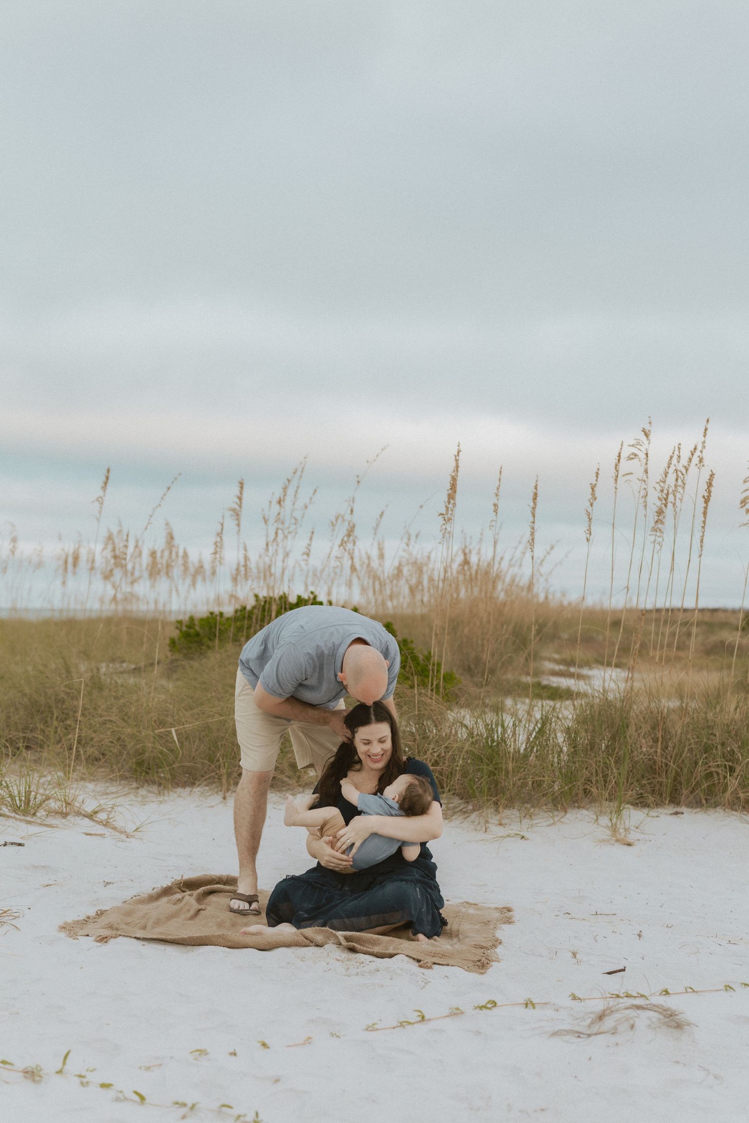 A couple shares intimate moments on a white sandy beach with sea oats swaying in the background.