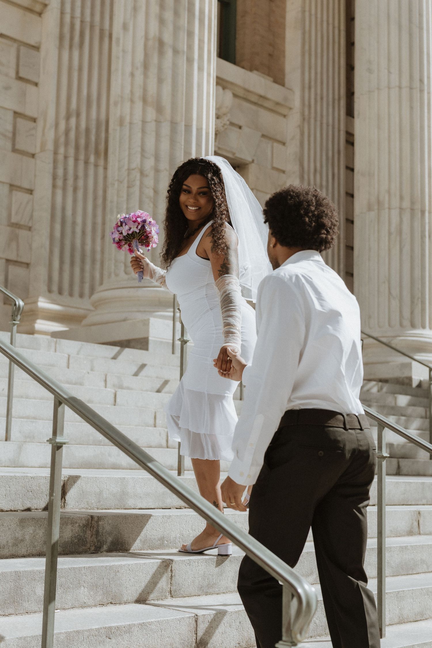 Group in formal attire walking up white marble steps with classical columns in the background.