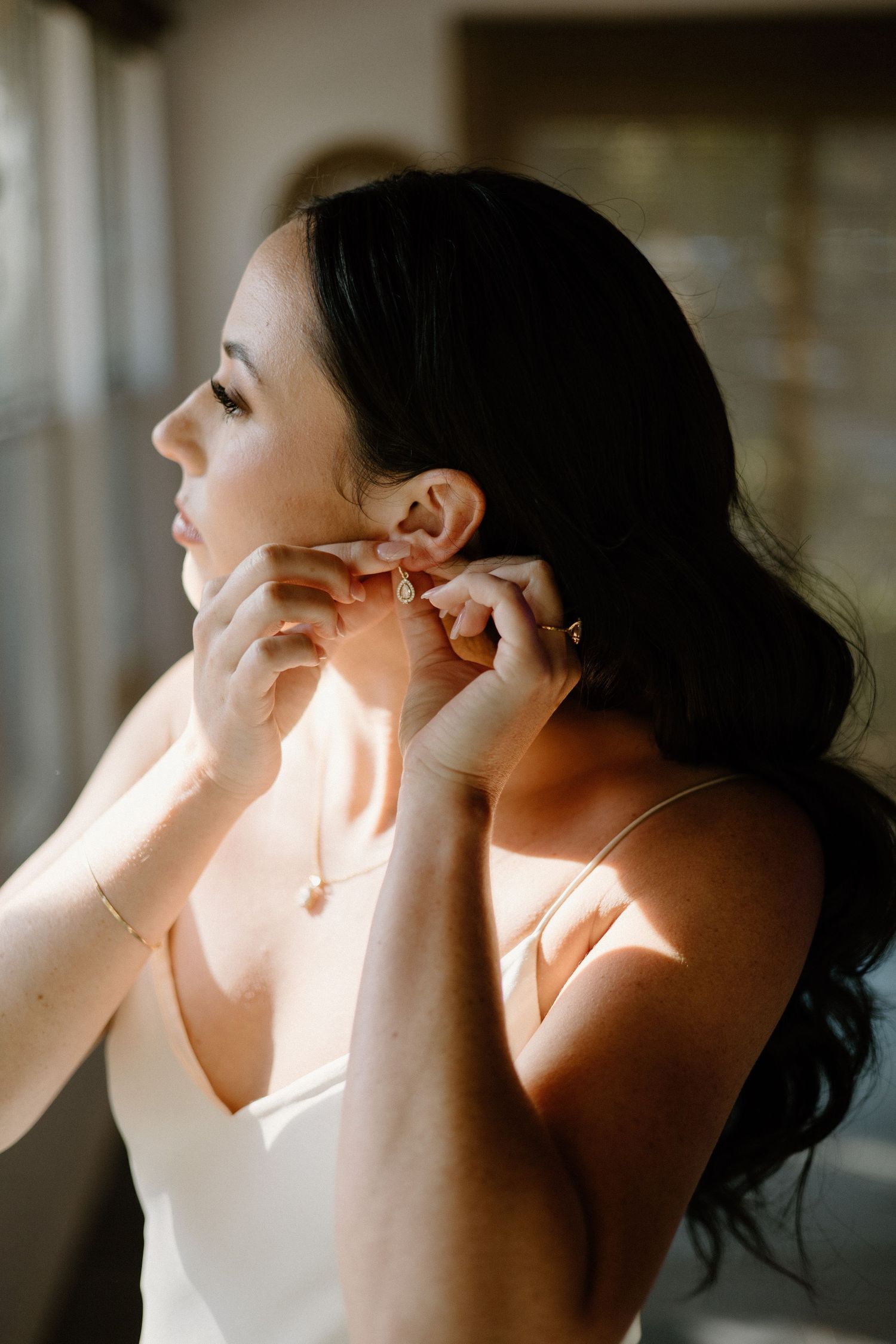 Side profile shots showing someone putting on delicate earrings in warm lighting.