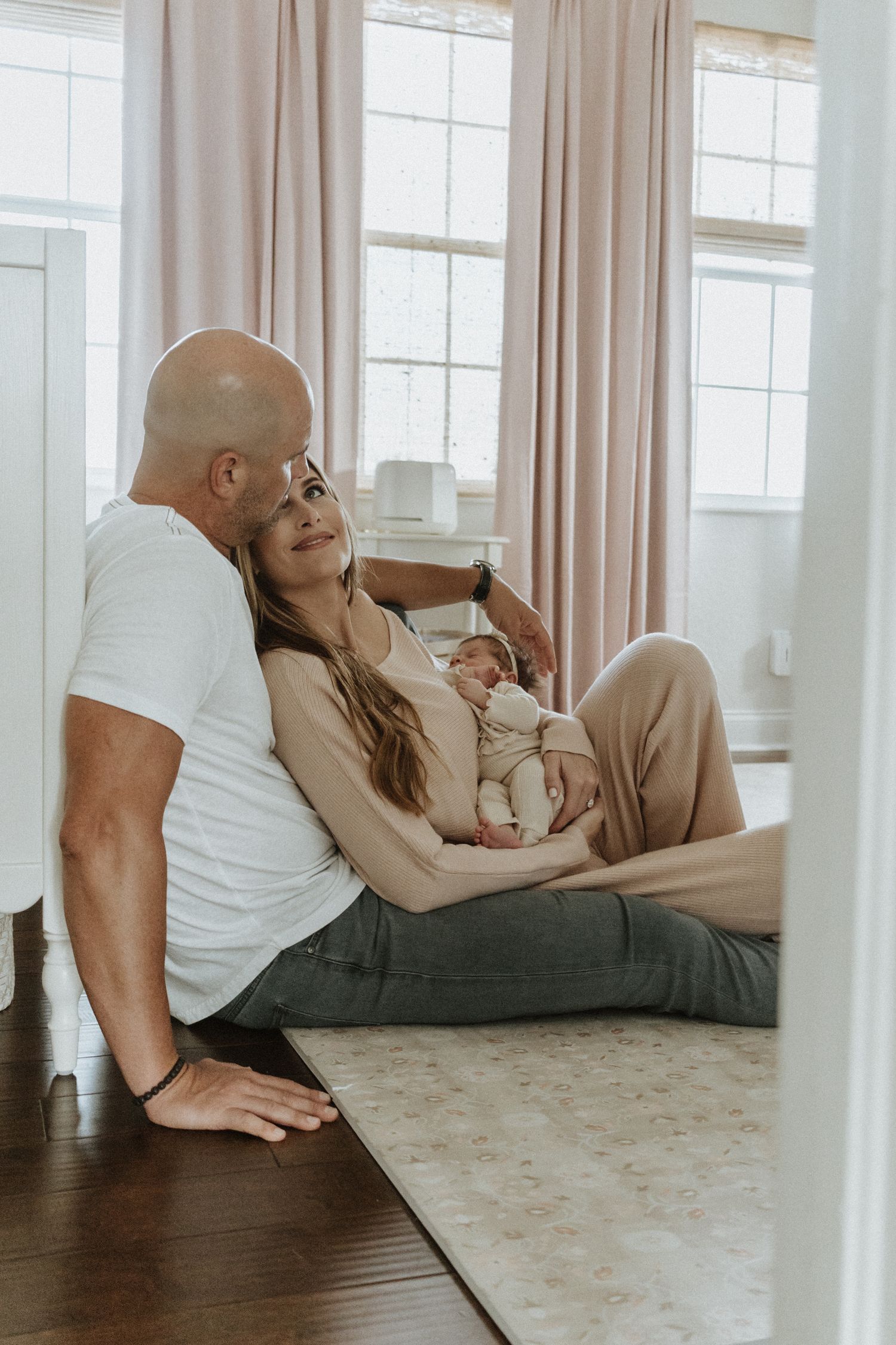Family relaxing together on floor at home with natural window light streaming in.