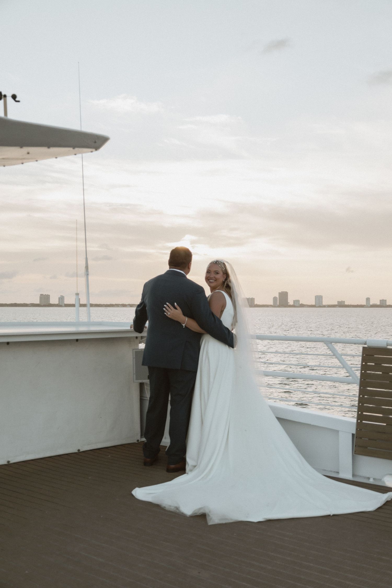 Couple embracing on a boat deck during sunset with city skyline in the background.