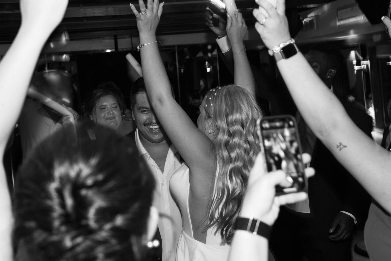 Crowd of wedding guests raising their hands in celebration on a dance floor.