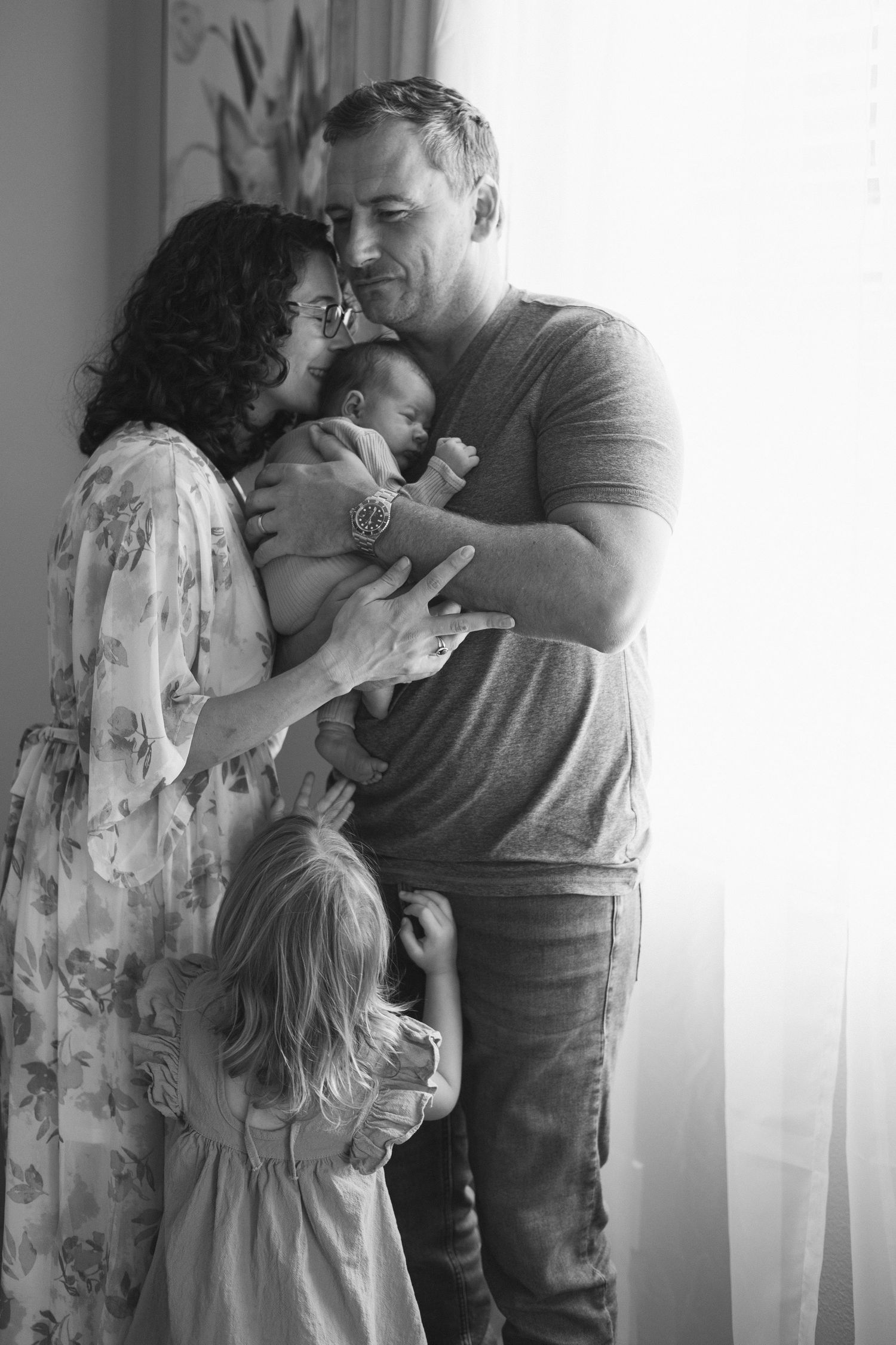 A tender family moment captured in black and white with soft window light.