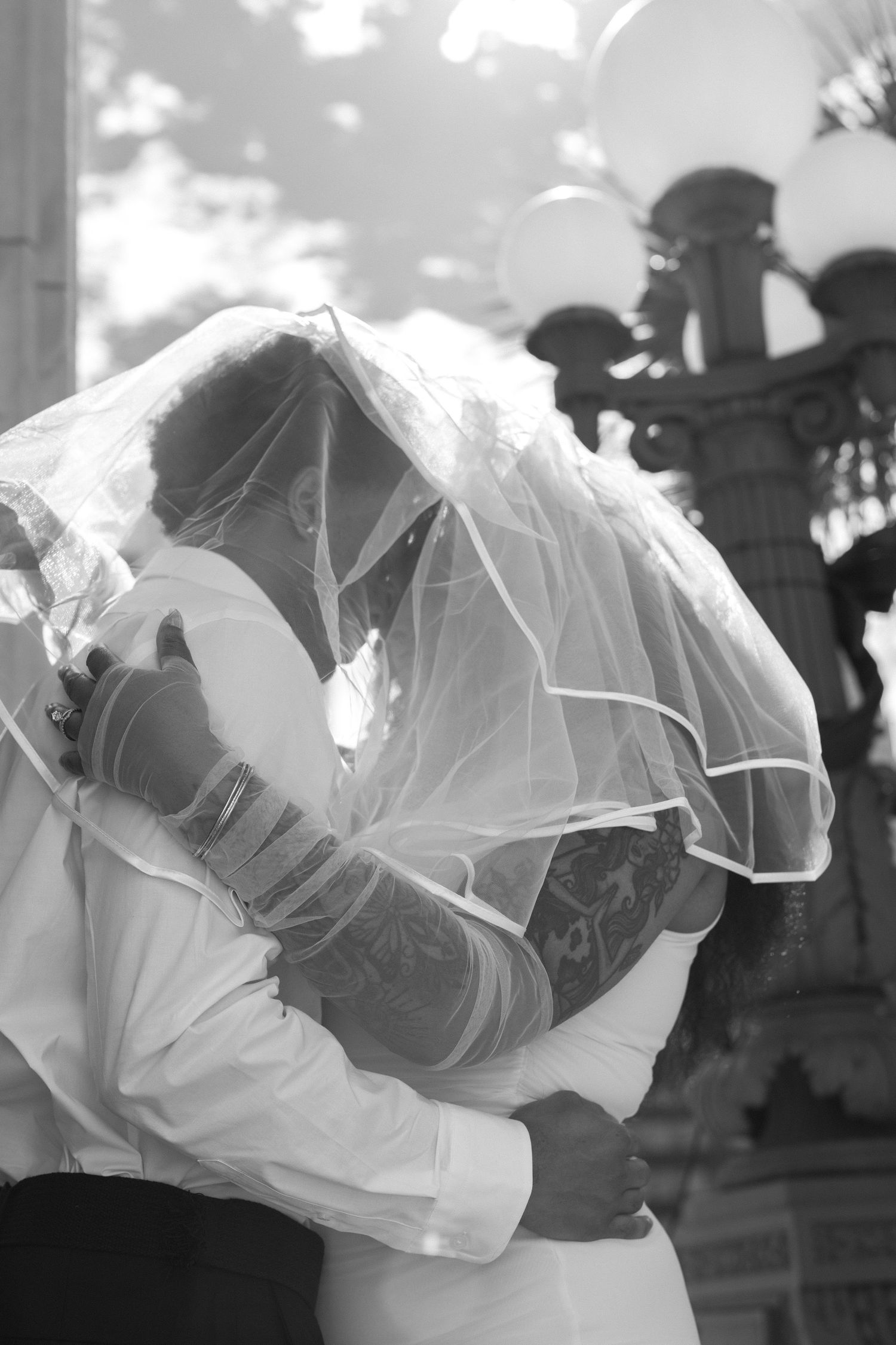 Four black and white photos show a romantic kiss between newlyweds under flowing white veils.