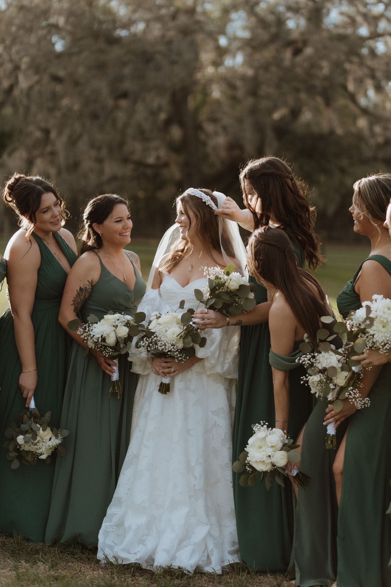 Bridesmaids in elegant green dresses gather around the bride for wedding photos.