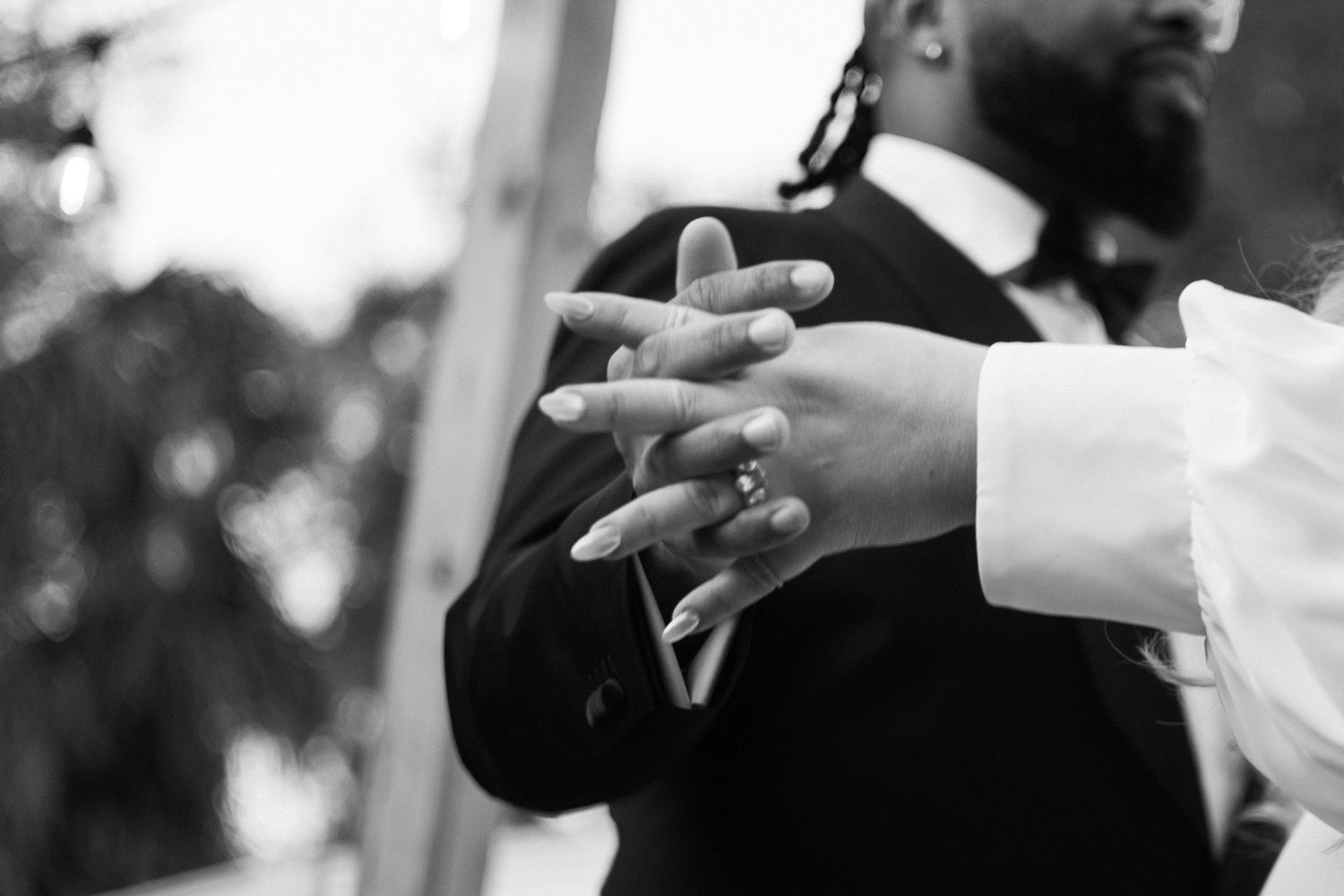 Close-up black and white photo of hands clasped together during wedding ceremony.